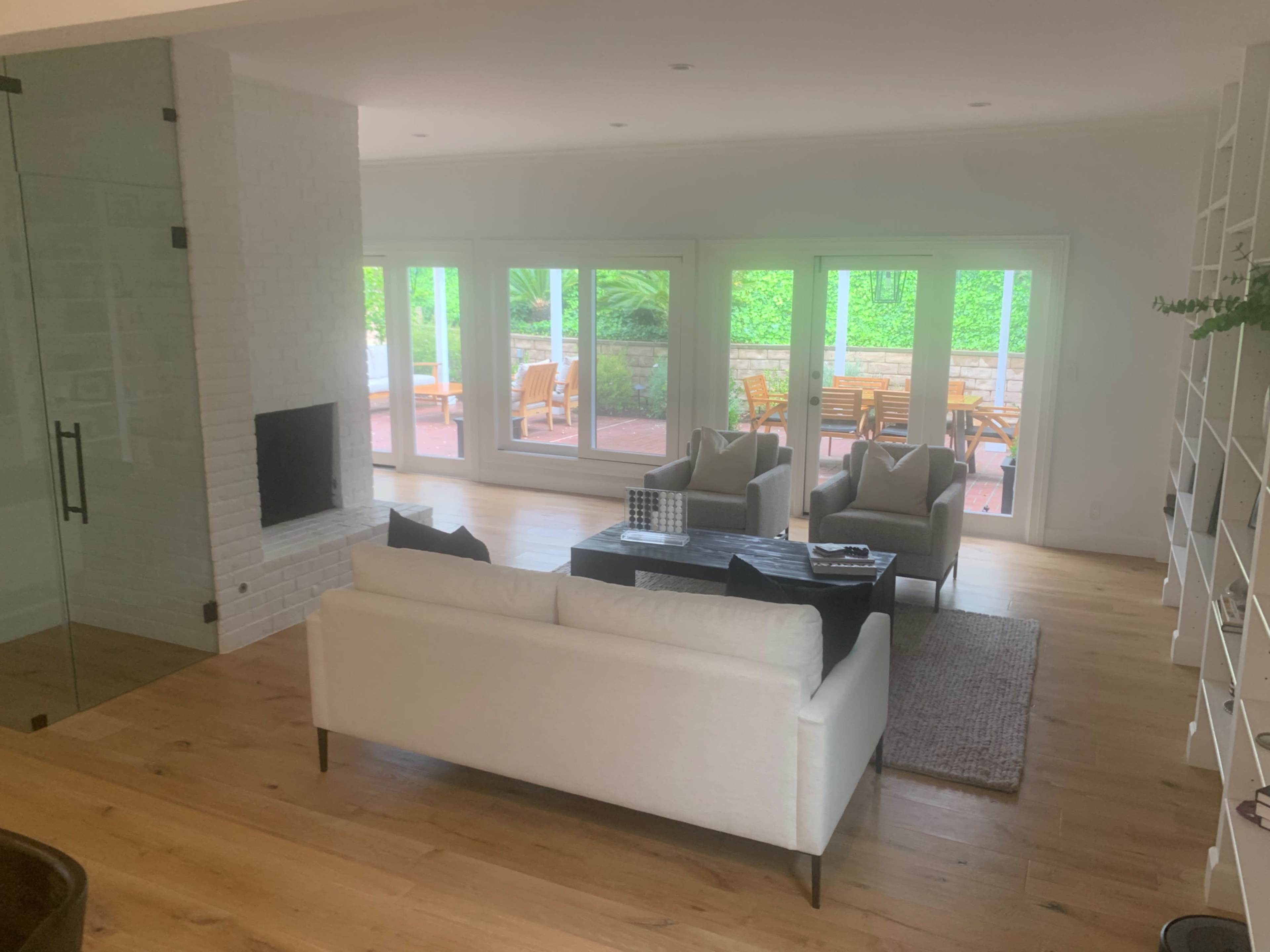 The image shows a modern living room with a white sofa, two armchairs, a coffee table, and large glass doors leading to a patio.