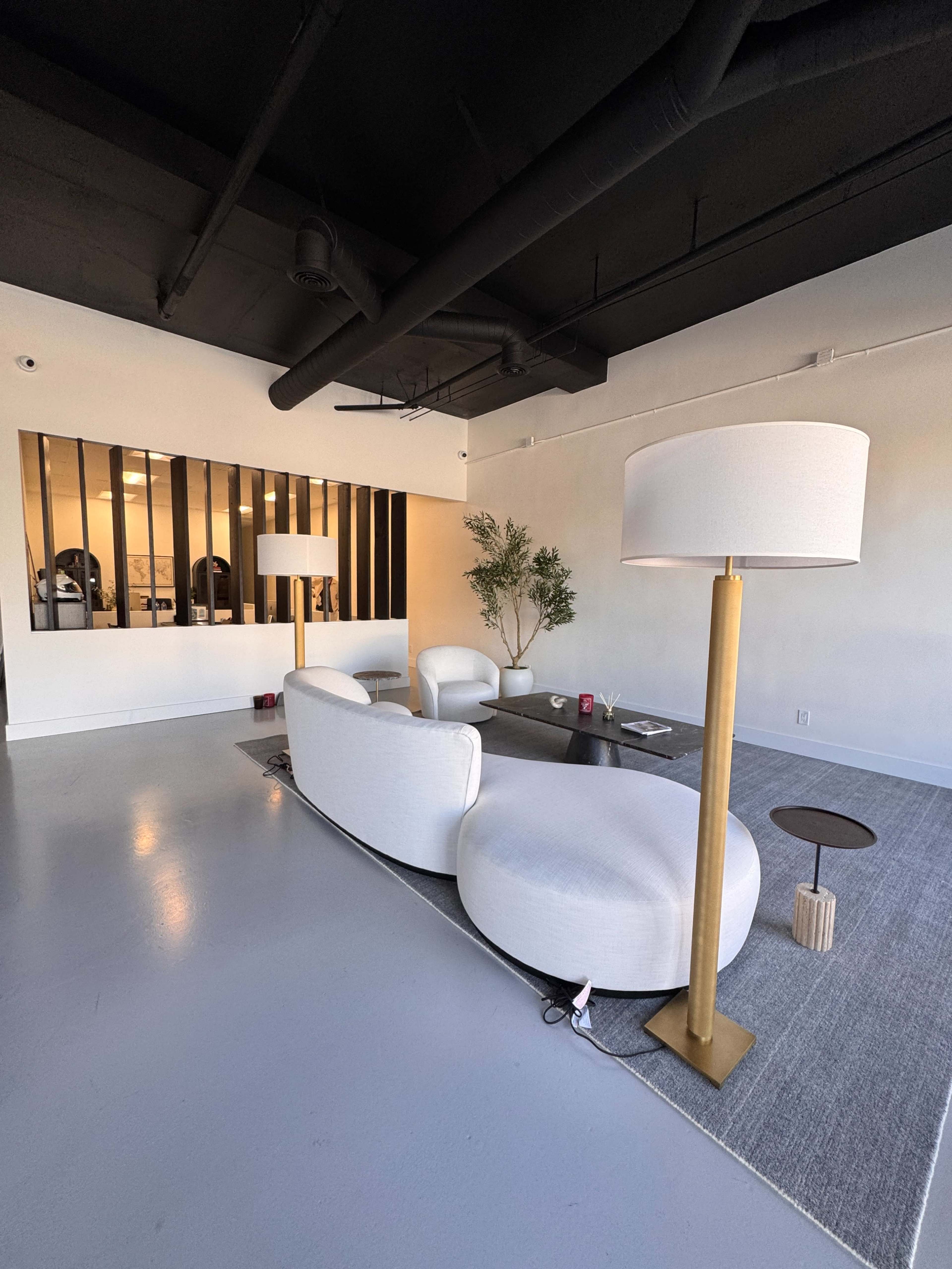 The image shows a modern interior space featuring a curved white sofa, two armchairs, a floor lamp, and a coffee table on a gray rug.
