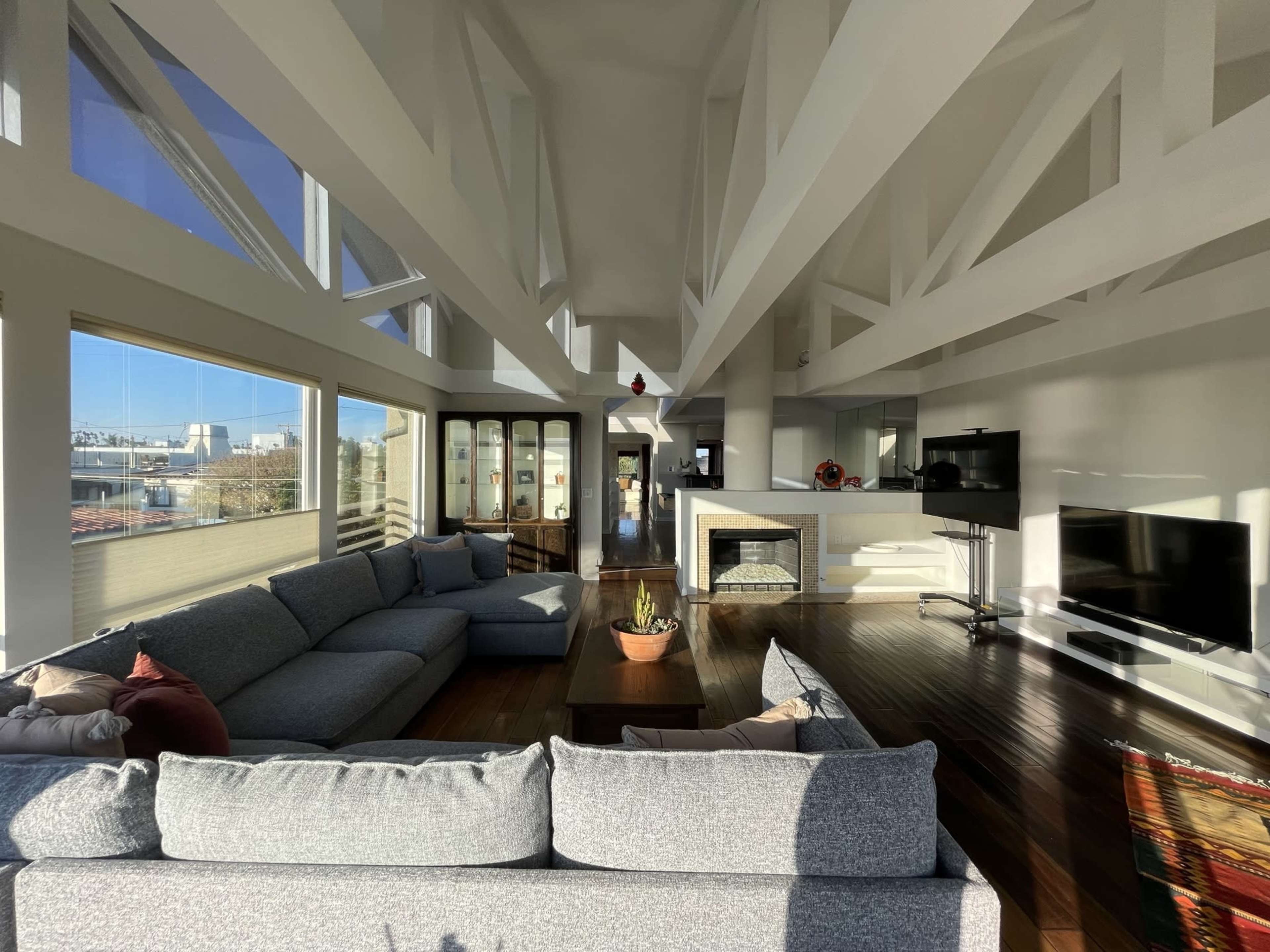 A spacious living room with a large sectional sofa, a coffee table, and a fireplace, featuring high ceilings and large windows that allow plenty of natural light.