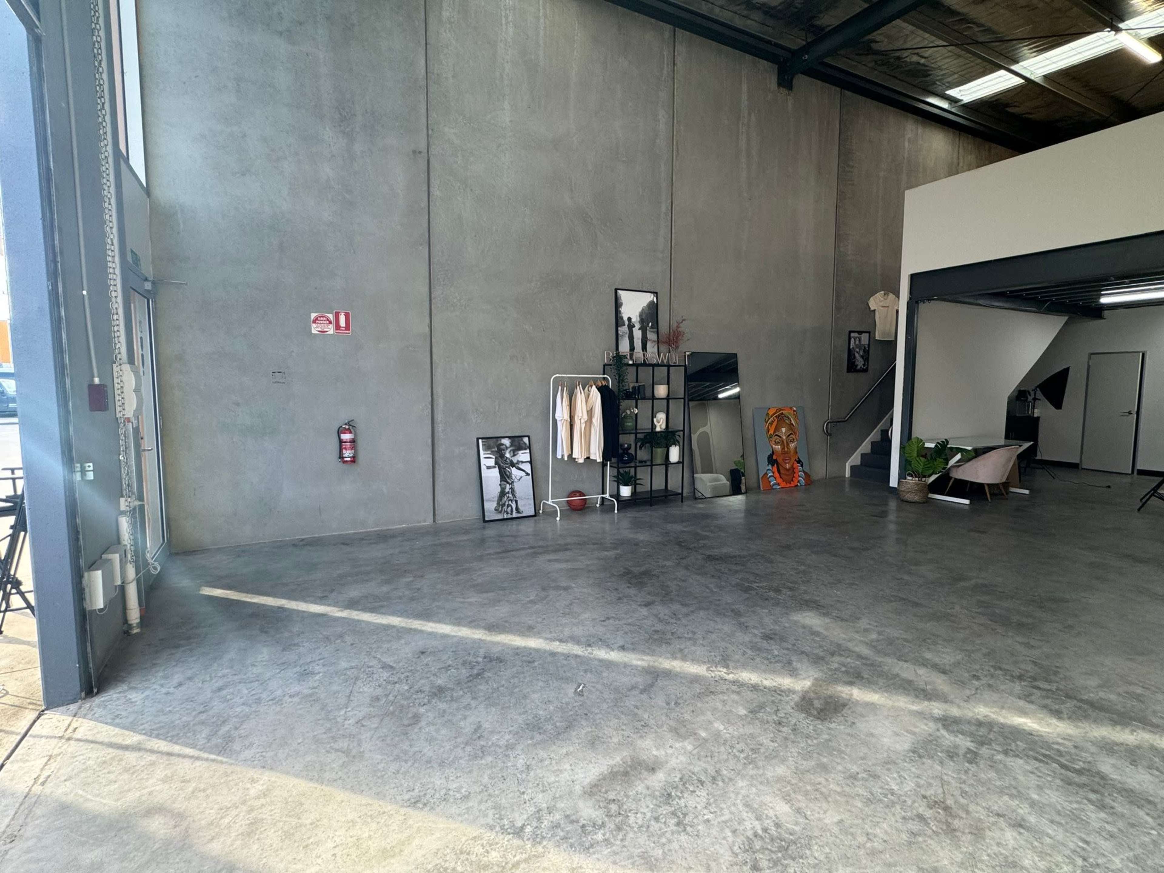 A spacious industrial-style interior with concrete flooring, a large open area, a staircase, and minimal furnishings.