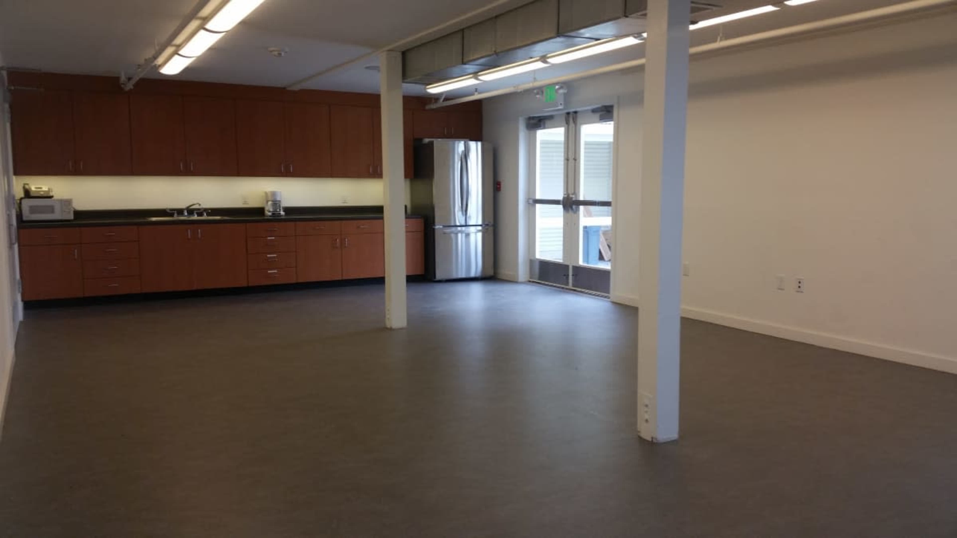 The image shows a spacious kitchen area with wooden cabinets, a stainless steel refrigerator, and a door leading outside.