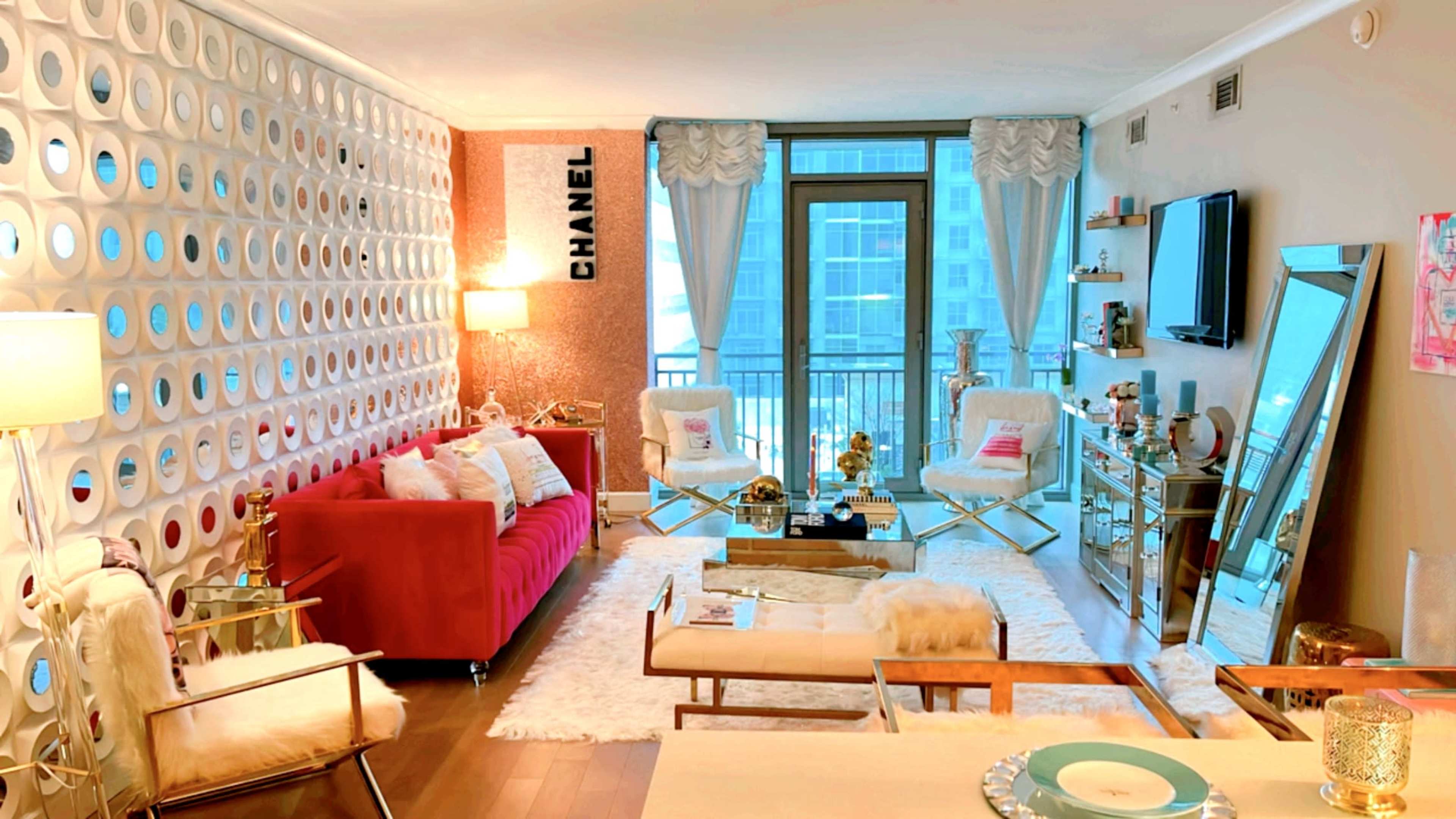 The living room features a red sofa against a decorative wall, a glass coffee table, and large windows overlooking a cityscape.