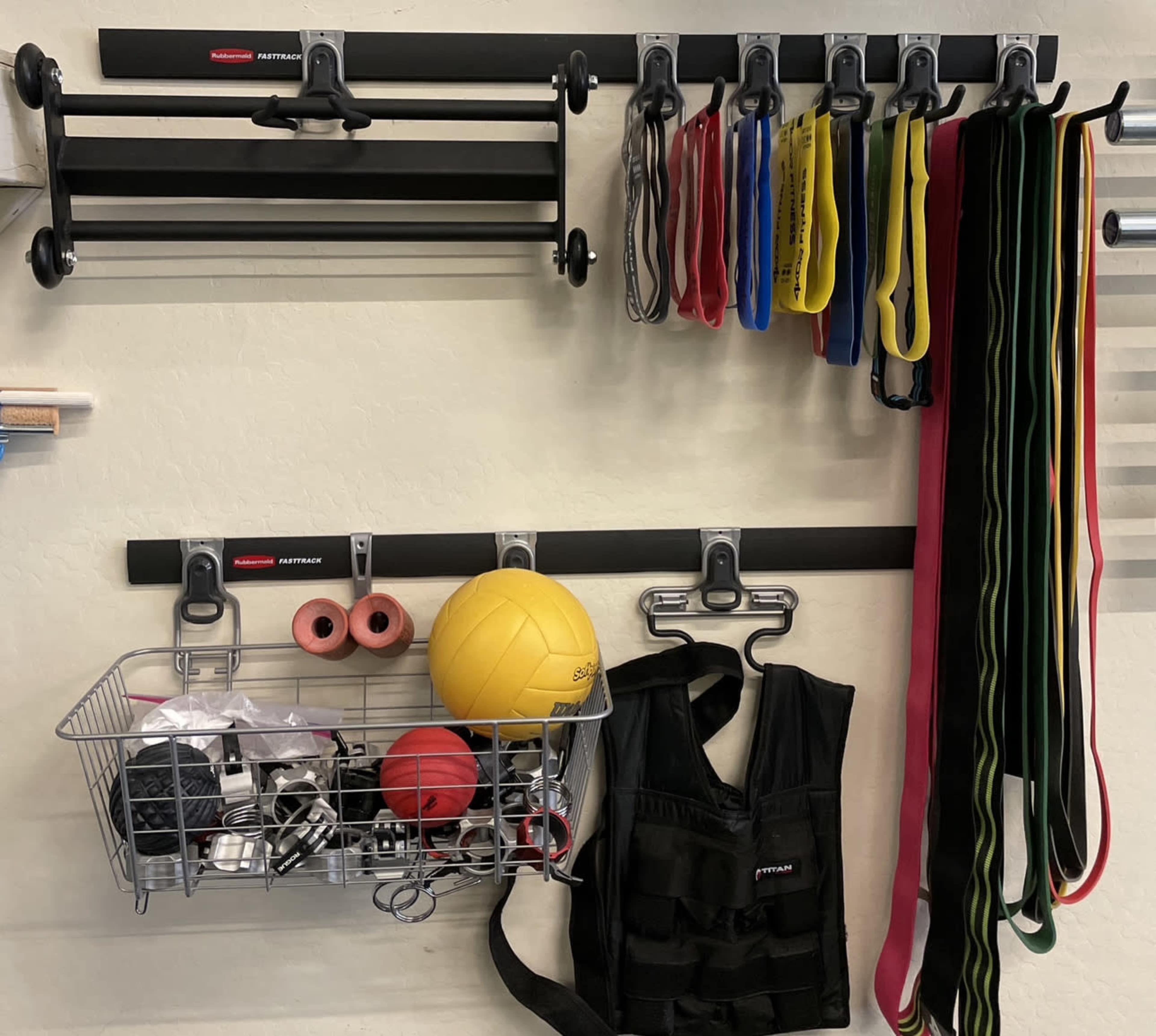 A wall-mounted organization system with exercise bands, a wire basket containing various fitness accessories, and a weighted vest.