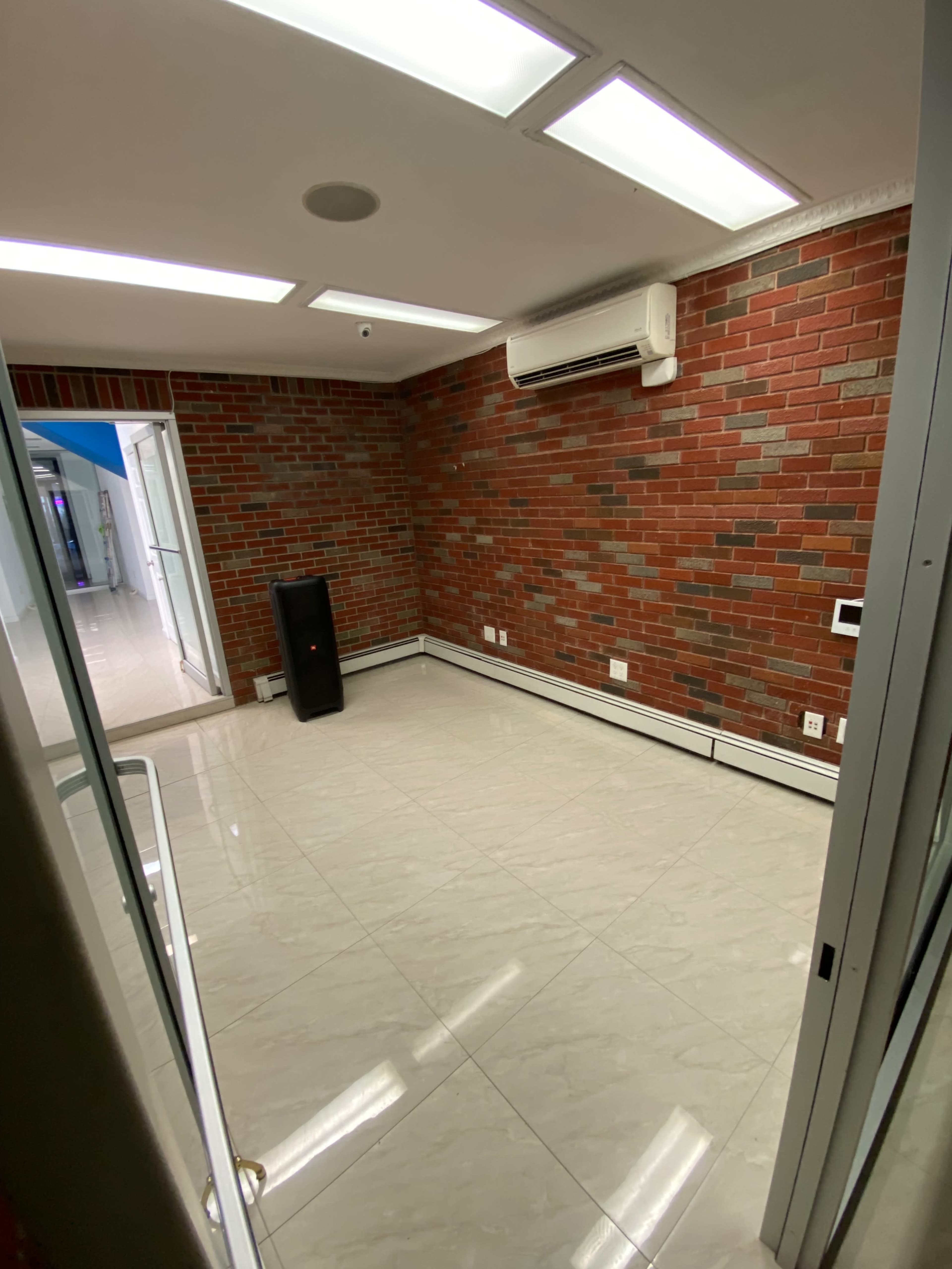 A small room with brick walls, tiled flooring, an air conditioning unit, and minimal furniture.