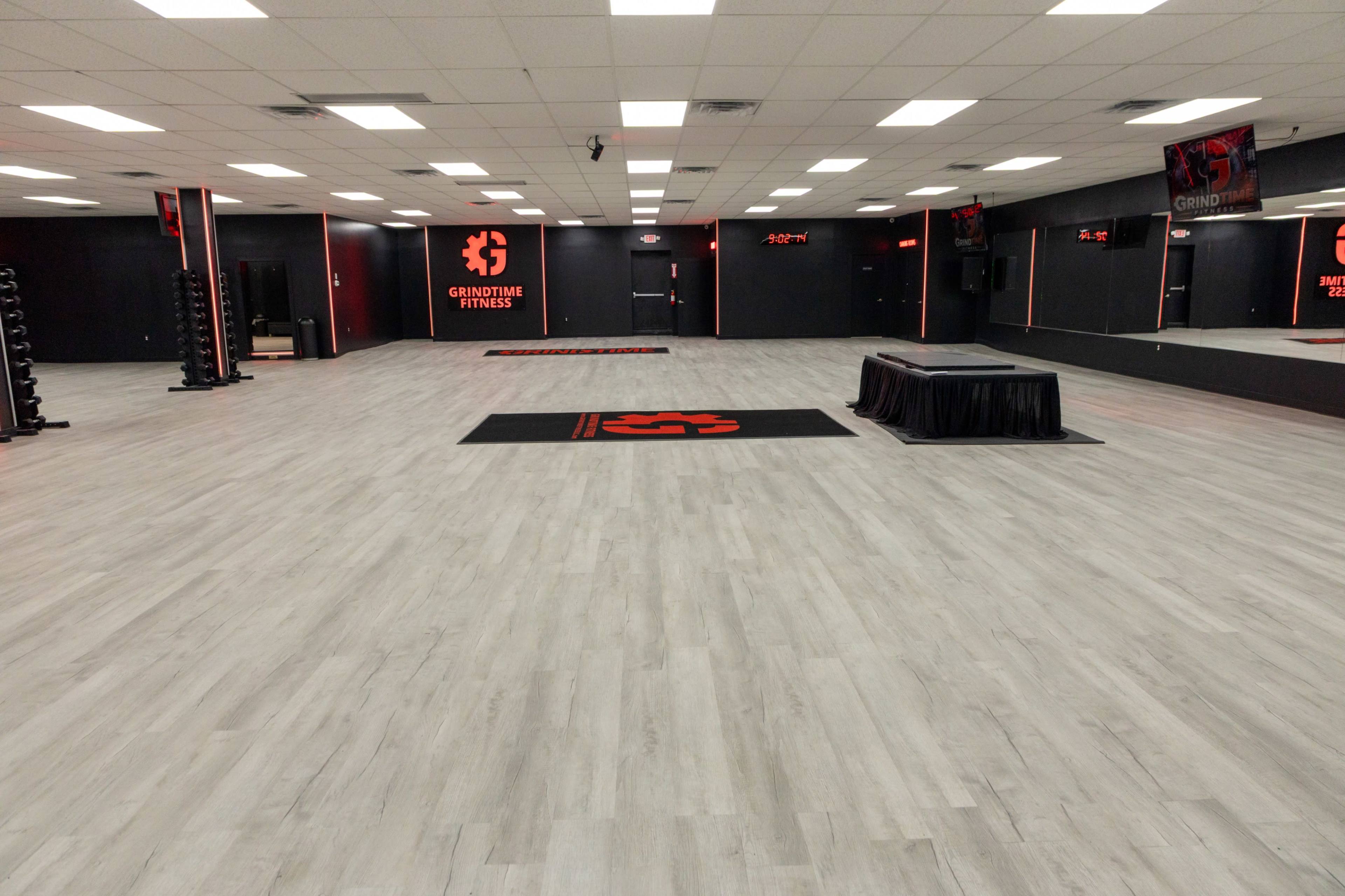 The image shows a spacious fitness studio with gray flooring and walls adorned with fitness-related branding and equipment along the sides.