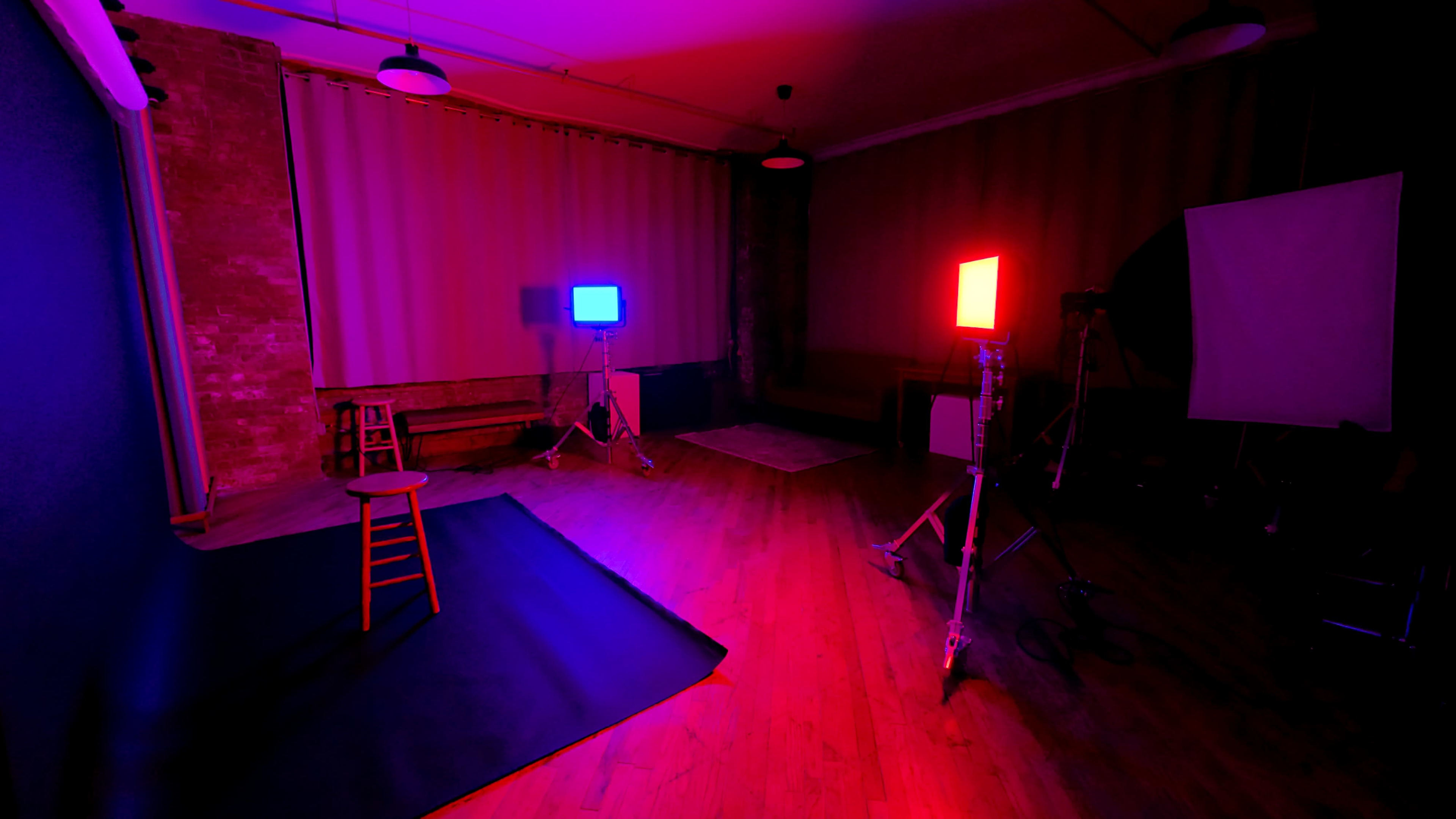 The scene features a dimly lit studio with a wooden stool on a black mat, illuminated by red and blue lights from two stands.