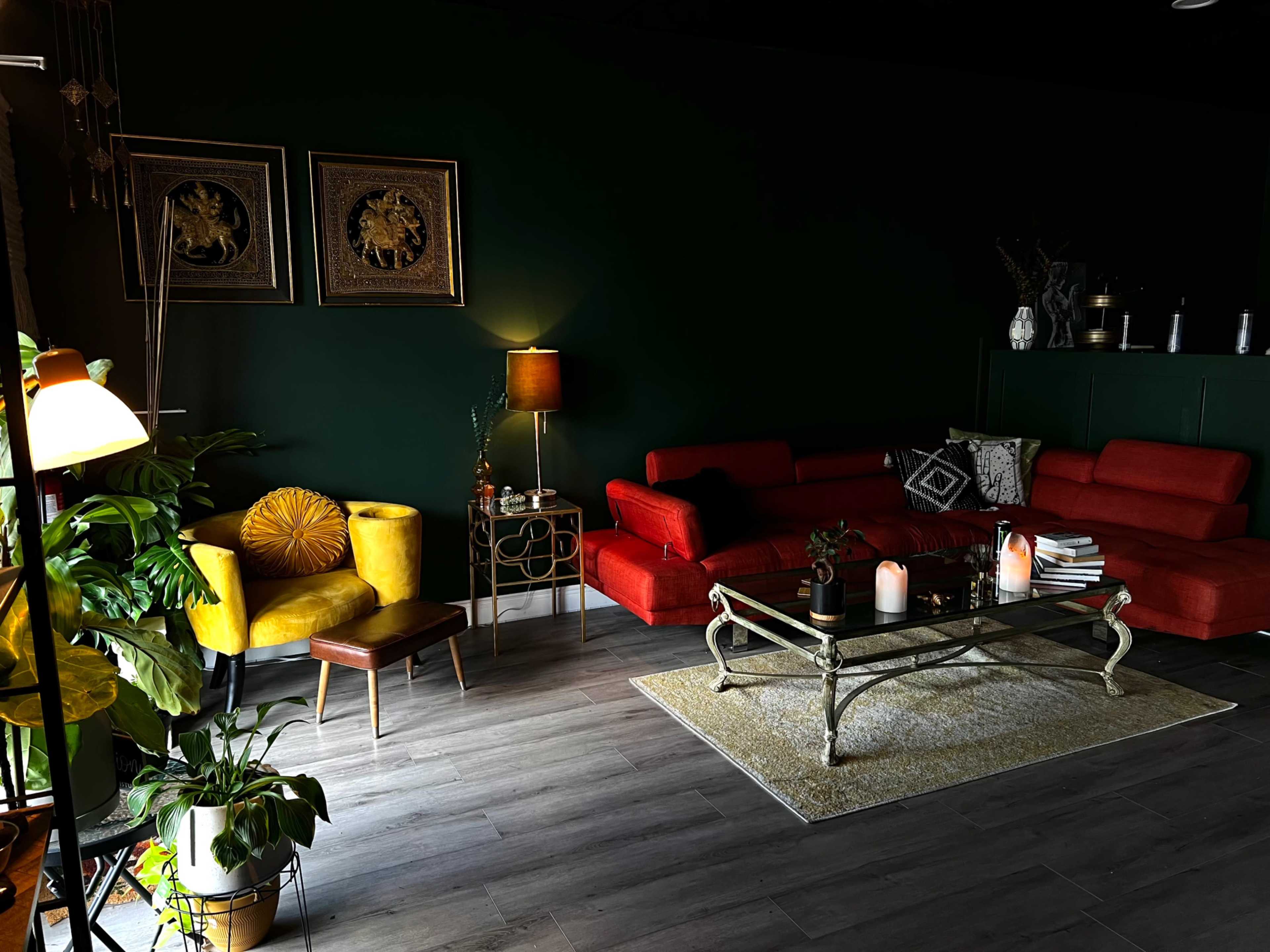 A modern living room with dark green walls, red sofas, a yellow armchair, a glass coffee table, and various decorative items.