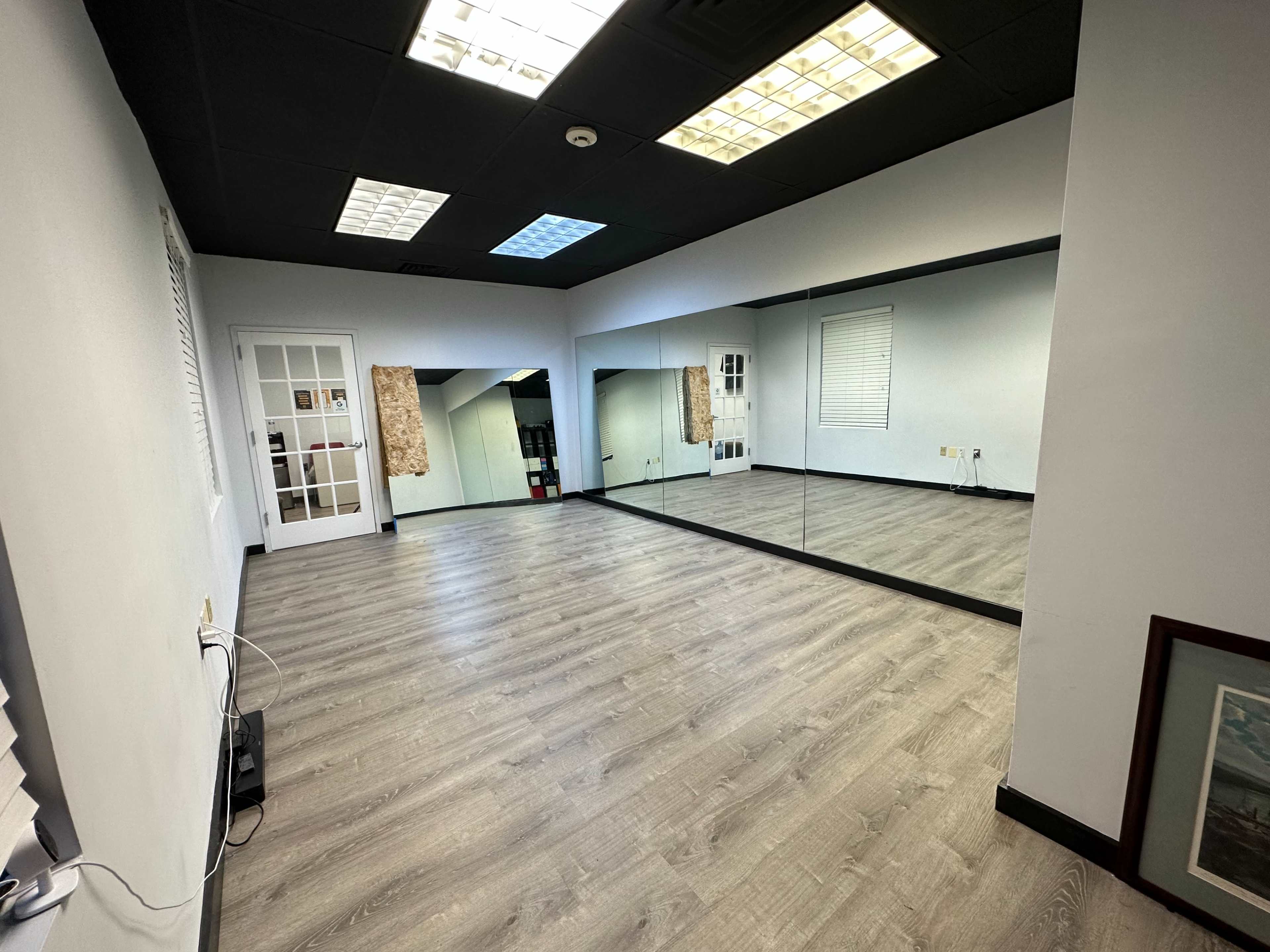 A spacious room with light-colored wooden flooring, a large mirror on one wall, and a door leading to another area.