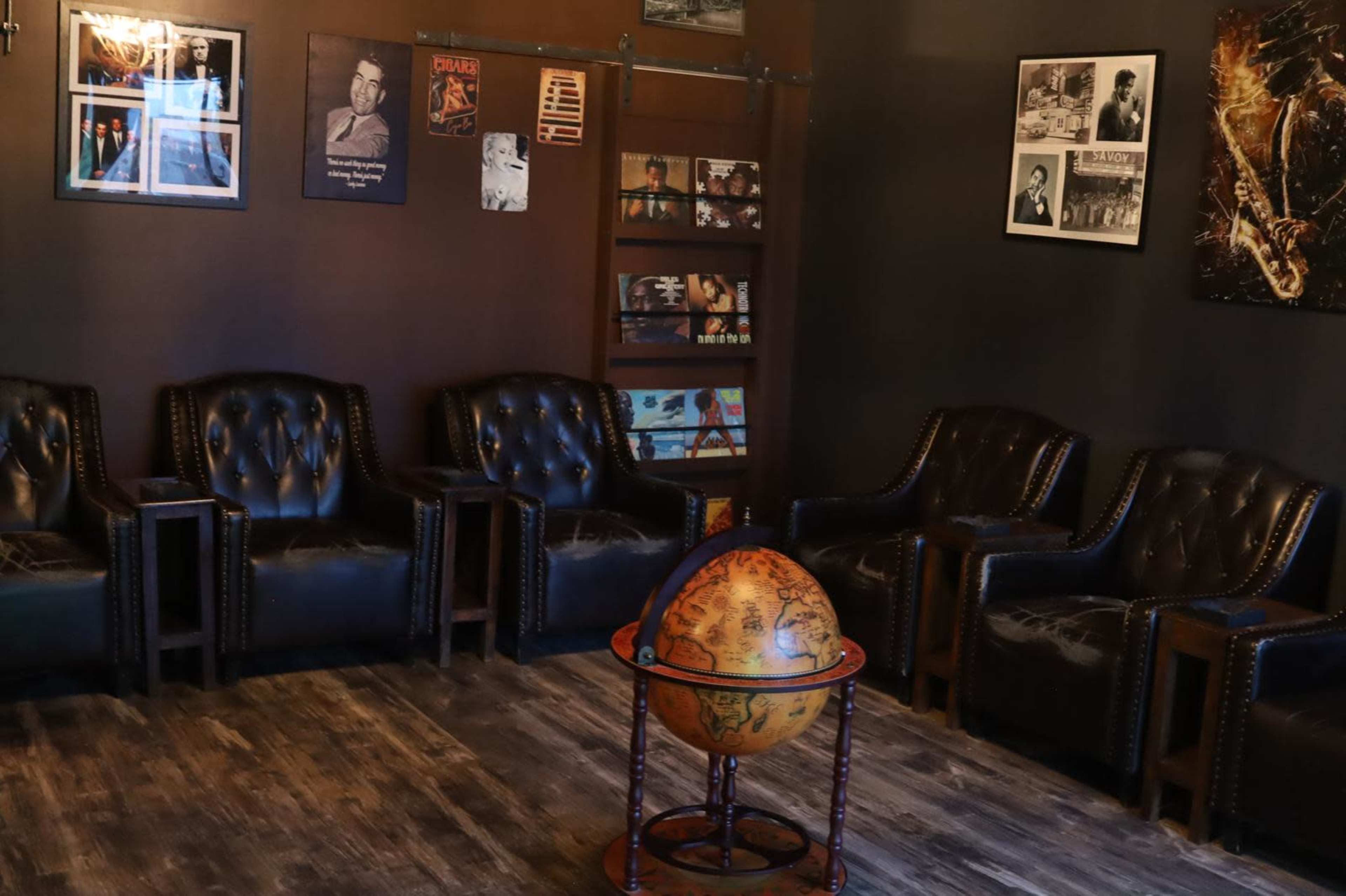 The image shows a cozy room with leather chairs arranged around a decorative globe and lined with photographs on the walls.