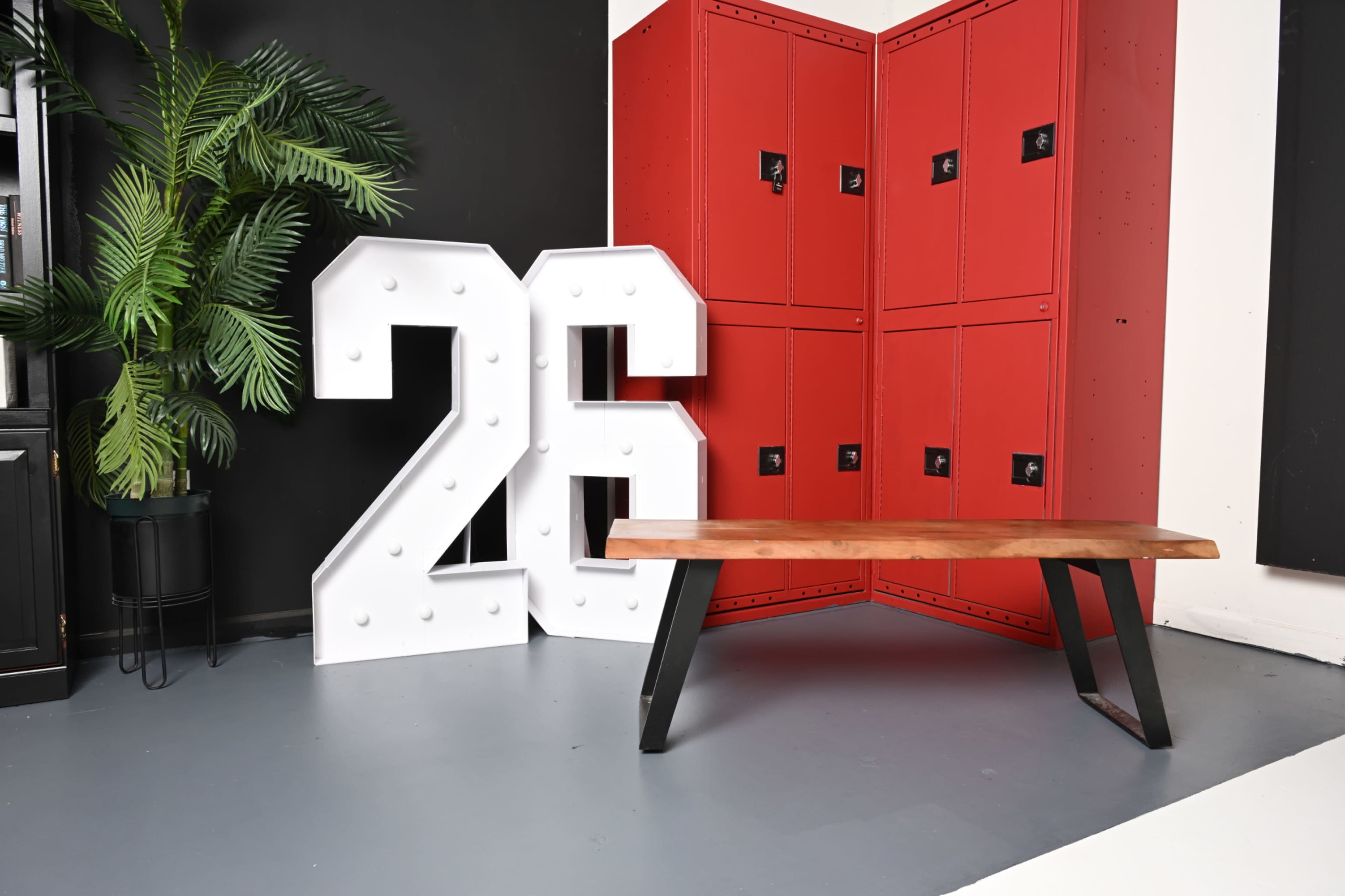 The image features a large white marquee number "26" next to red lockers and a wooden bench with black metal legs in a minimalistic interior setting.