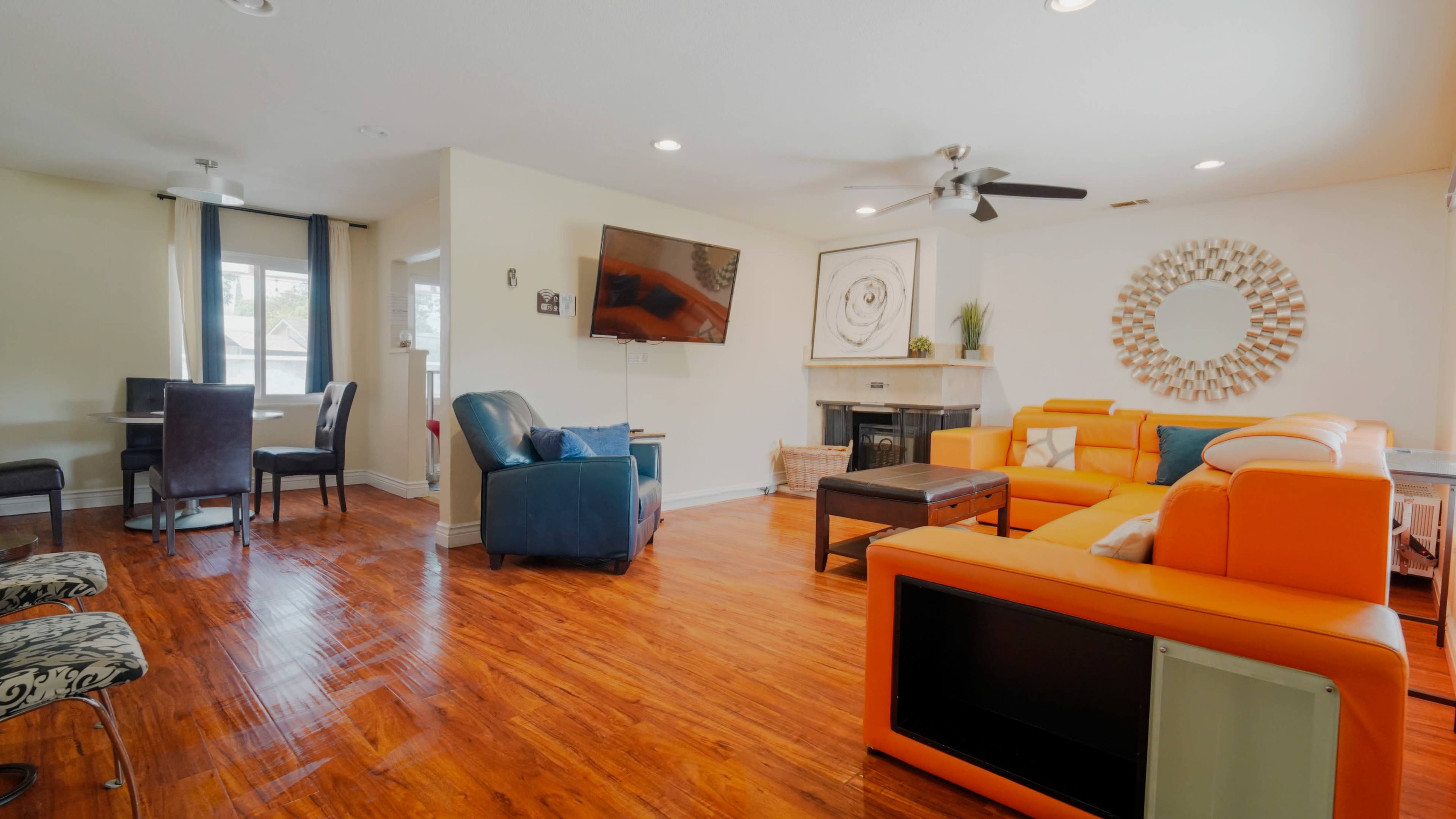 The living room features an orange sectional sofa, a blue armchair, a television mounted on the wall, and a fireplace with a mirror above it.