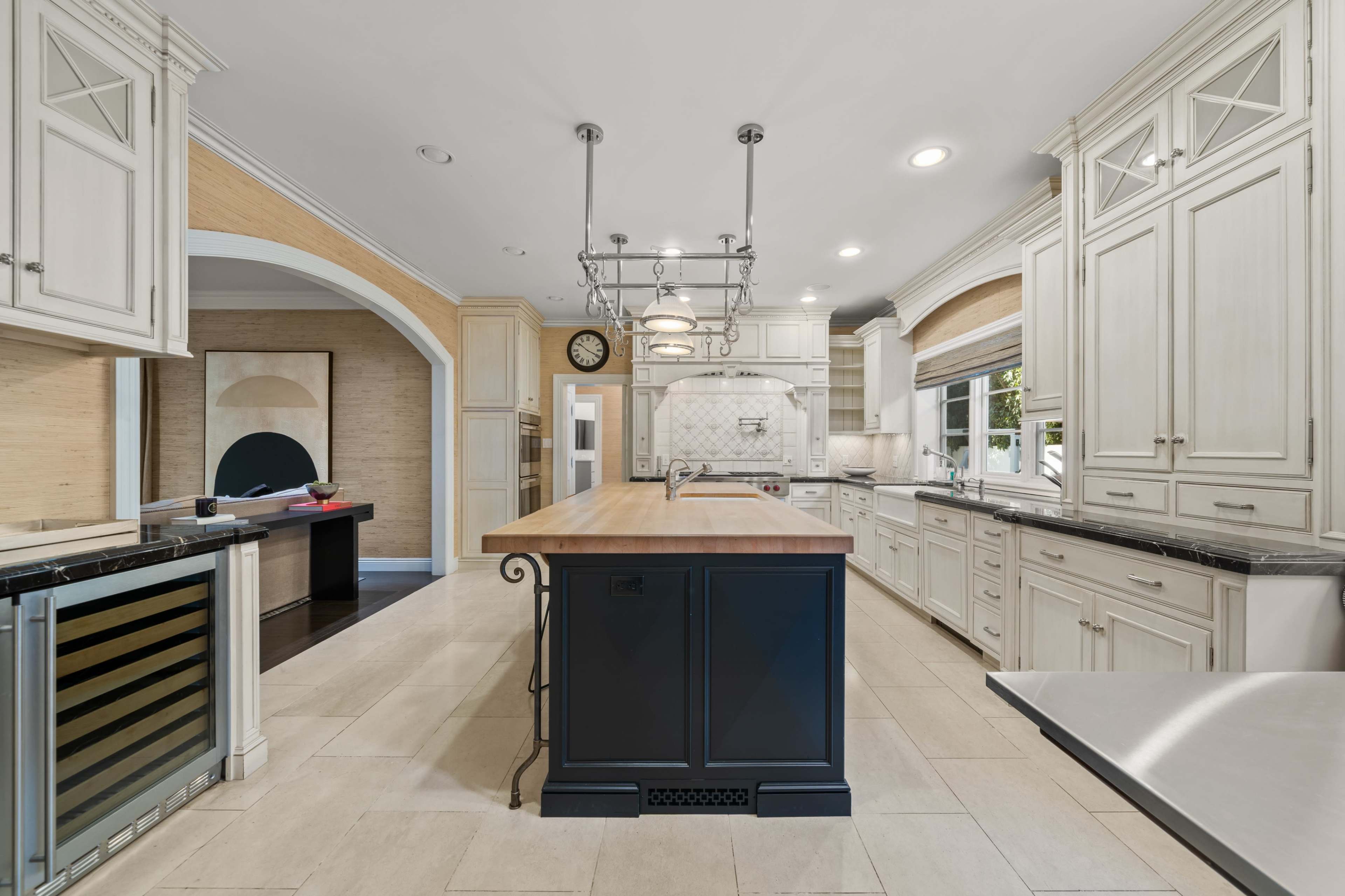 The image shows a spacious kitchen featuring an island with a wooden countertop, white cabinetry, and modern appliances.