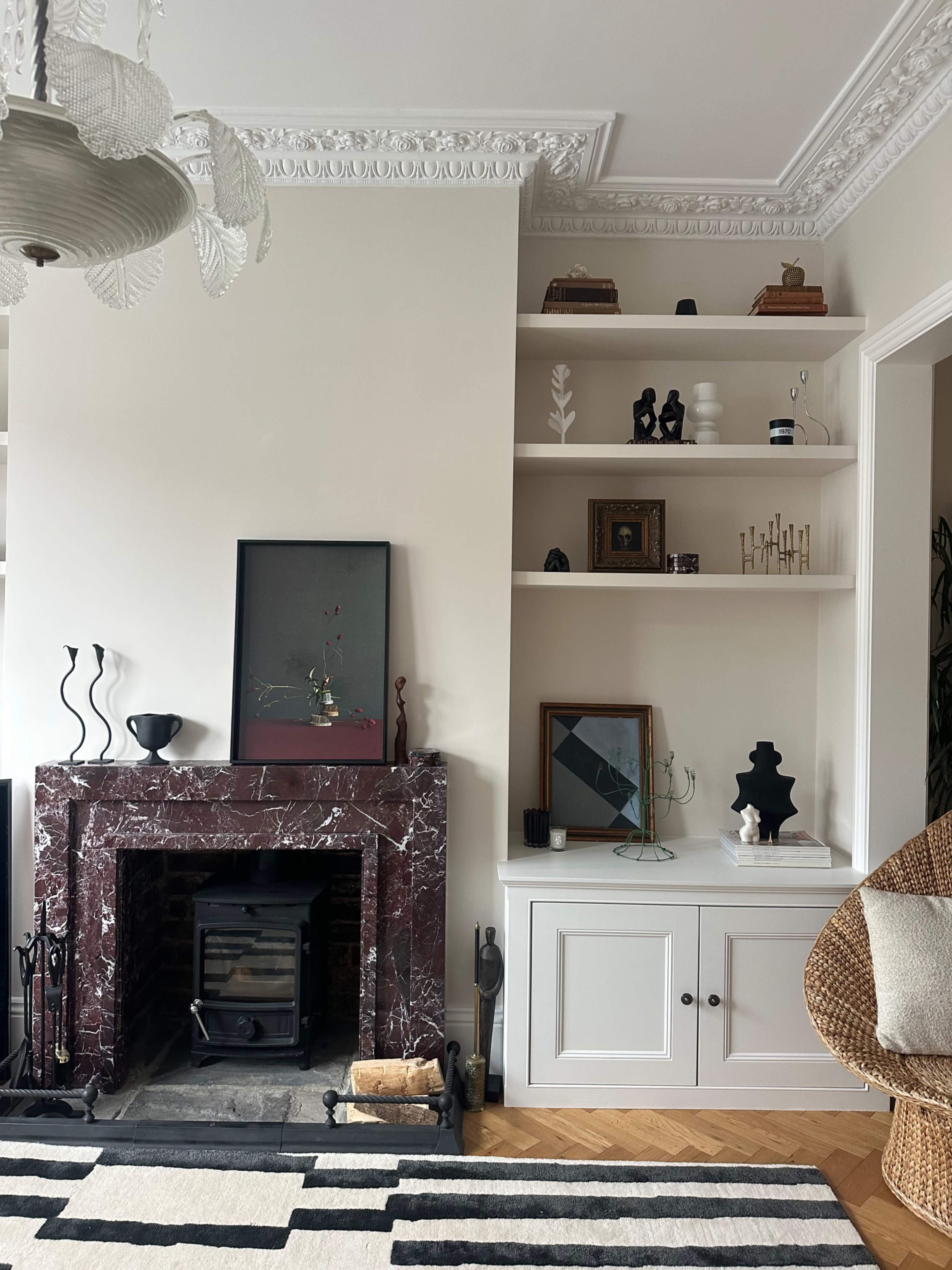 The image shows a living room with a marble fireplace, built-in shelves displaying various decorative items, and a patterned area rug on the wooden floor.