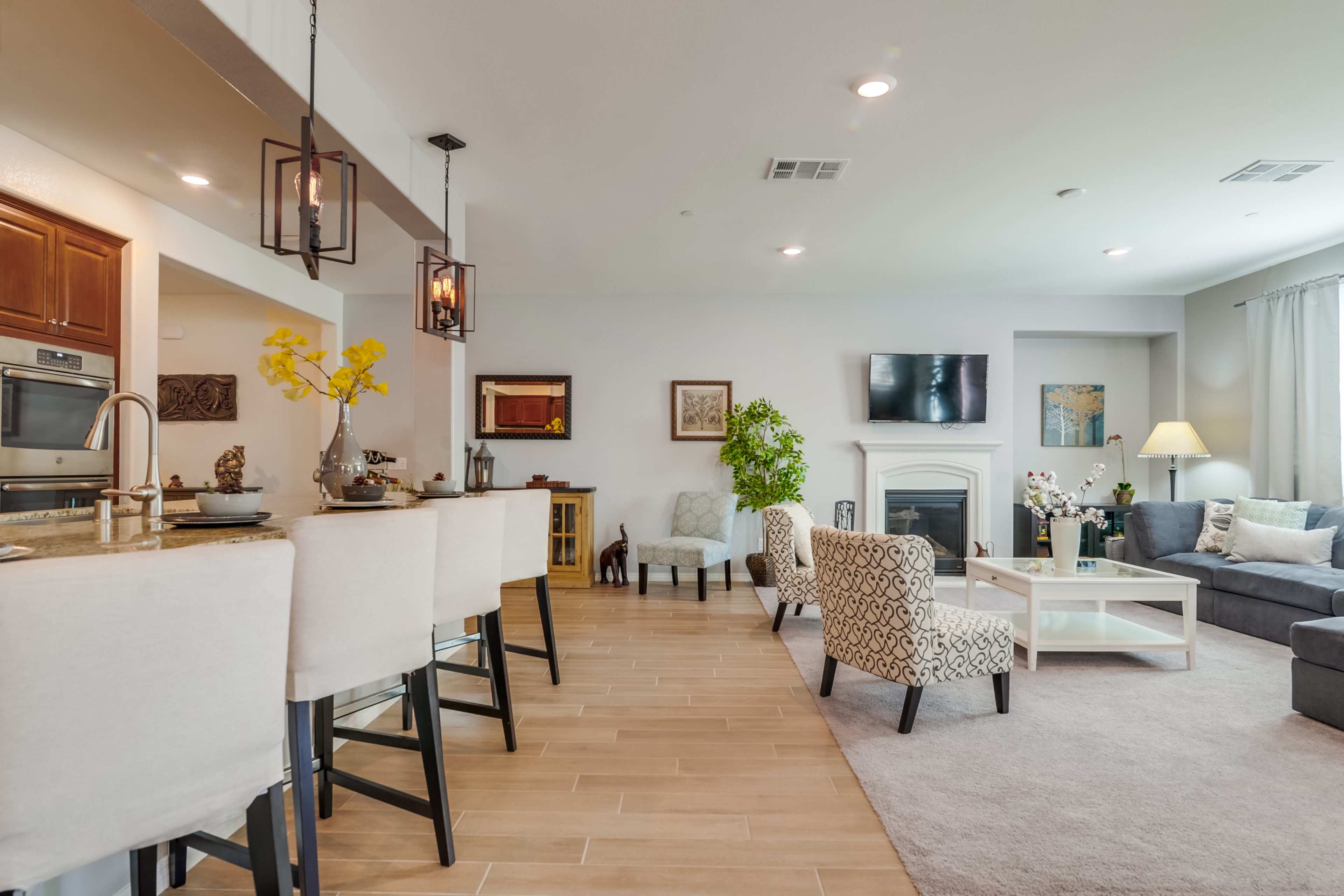 A modern living room with an open layout featuring a kitchen bar, seating areas, and a fireplace.