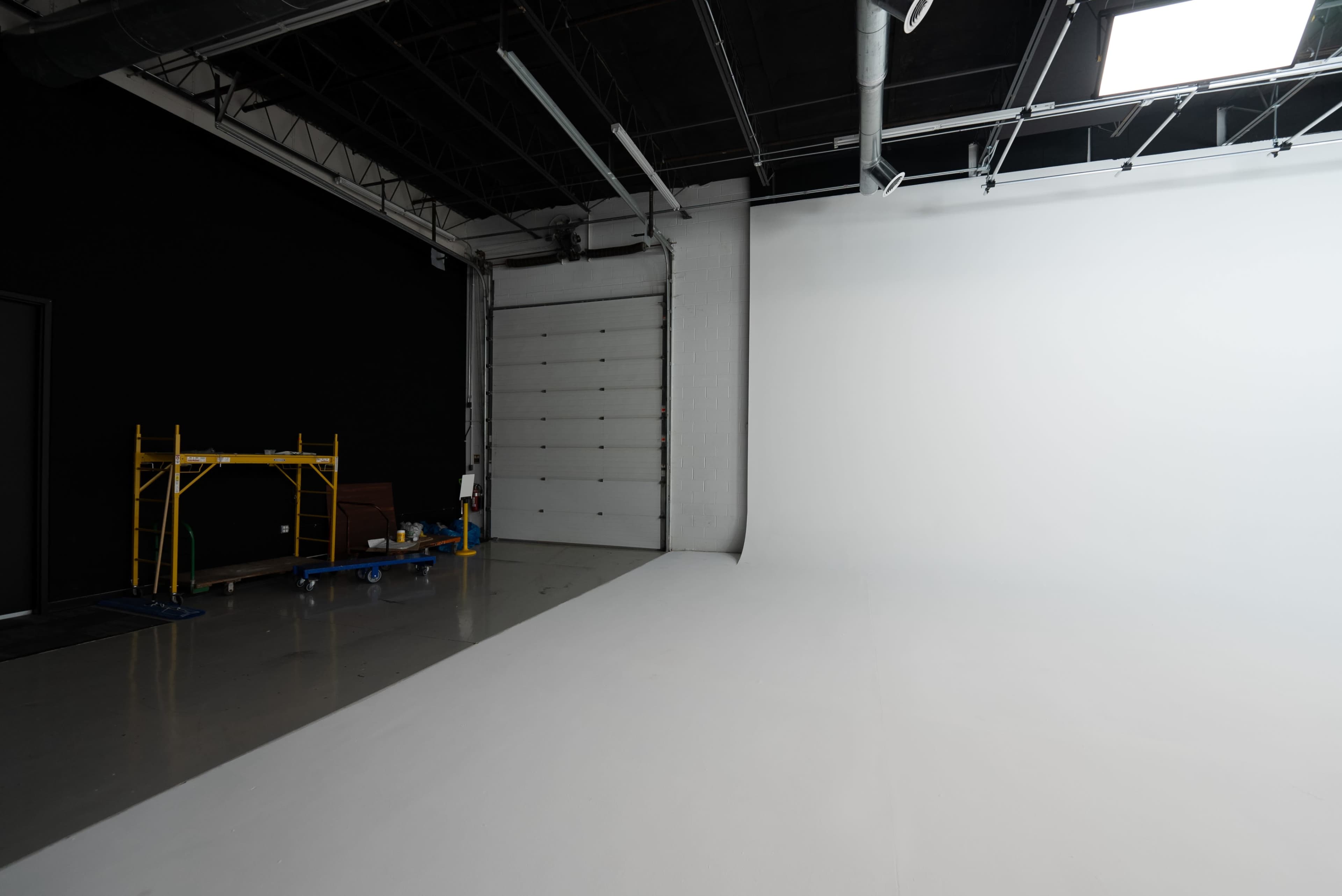 The image shows an empty photo studio with a white backdrop and a black wall.