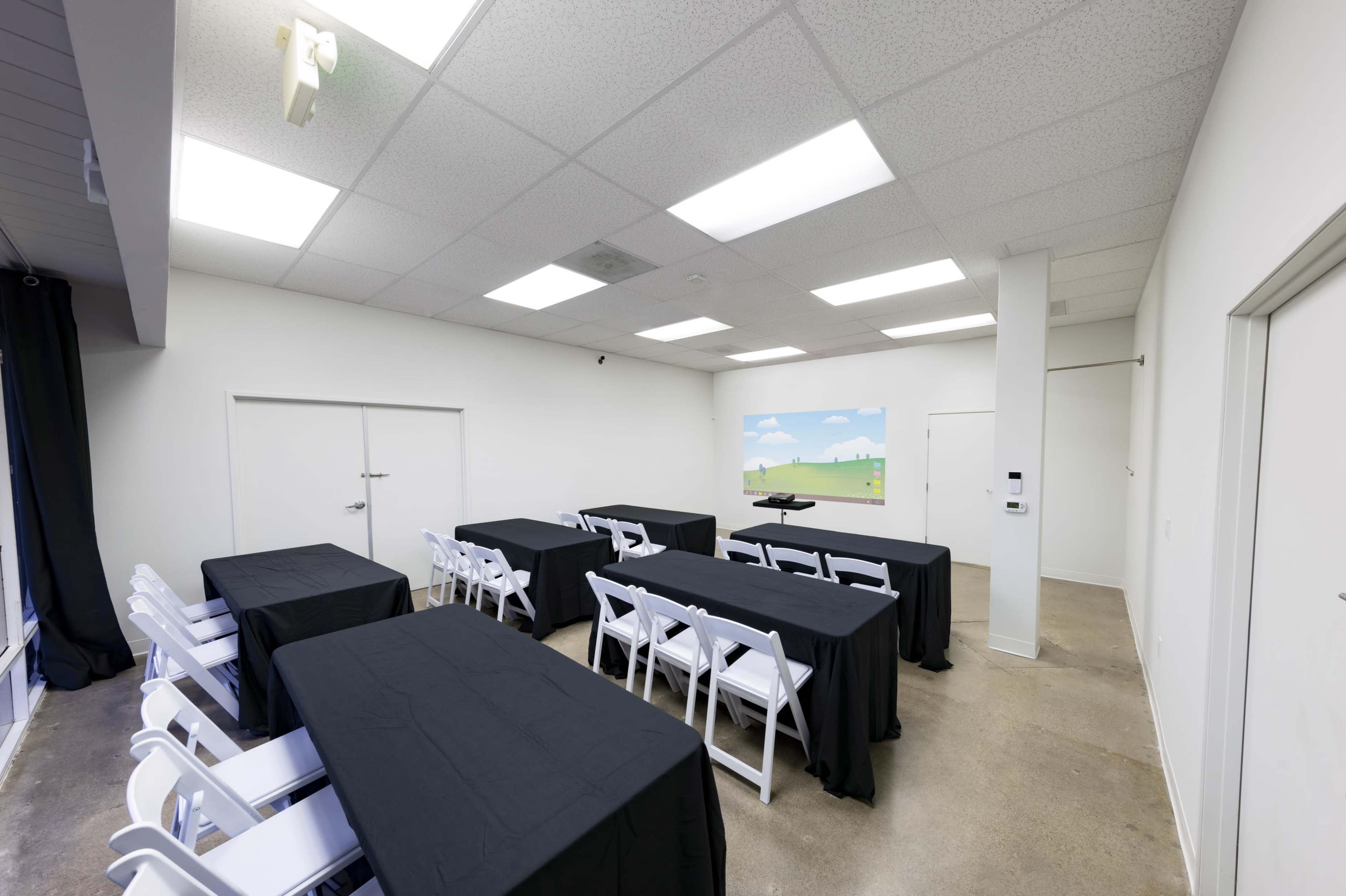 A conference room features several tables covered with black tablecloths, white folding chairs, and a projection screen displaying a landscape scene.