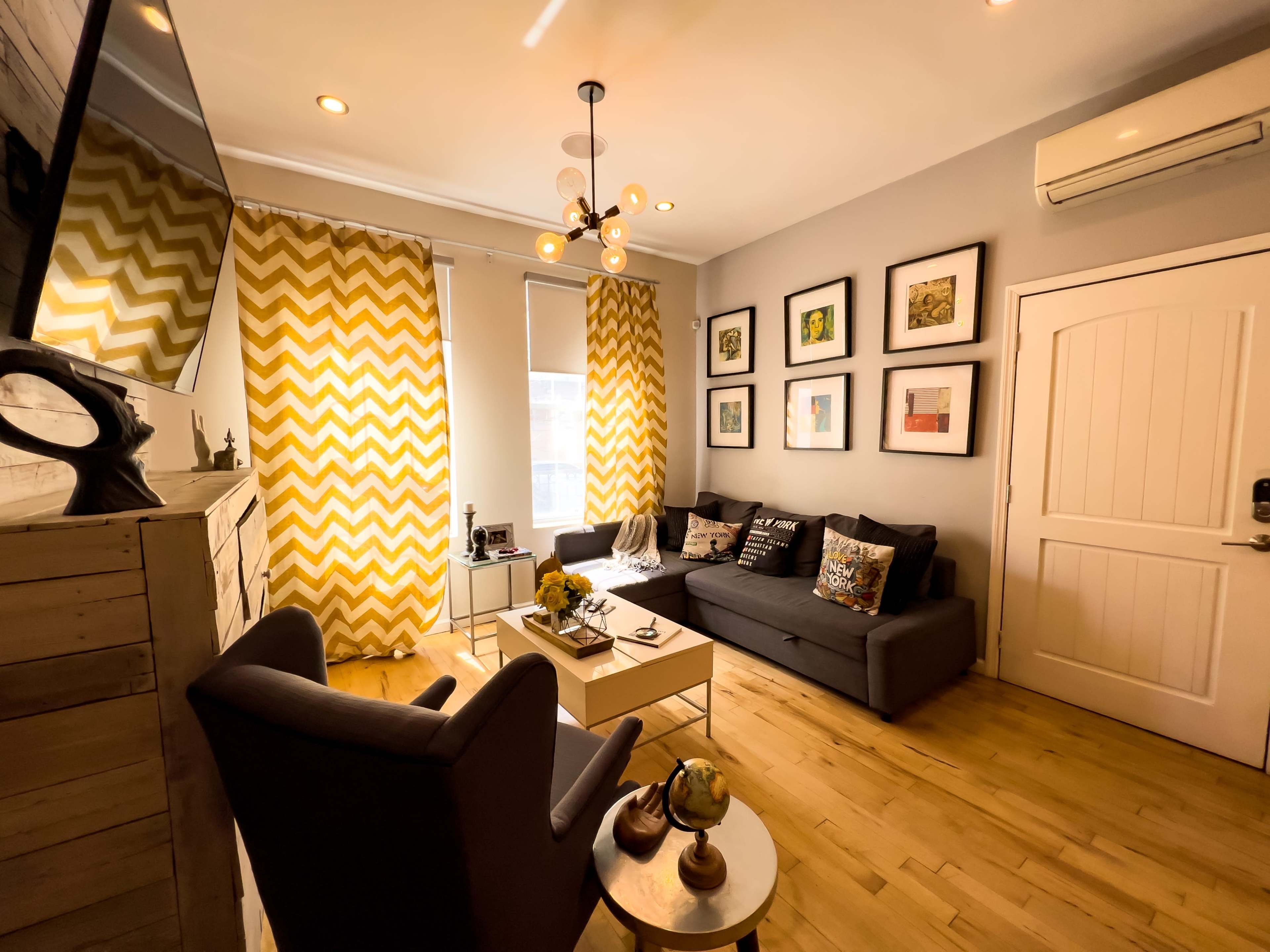 A cozy living room with a dark sofa, two armchairs, a decorative coffee table, and yellow chevron-patterned curtains framing a window.