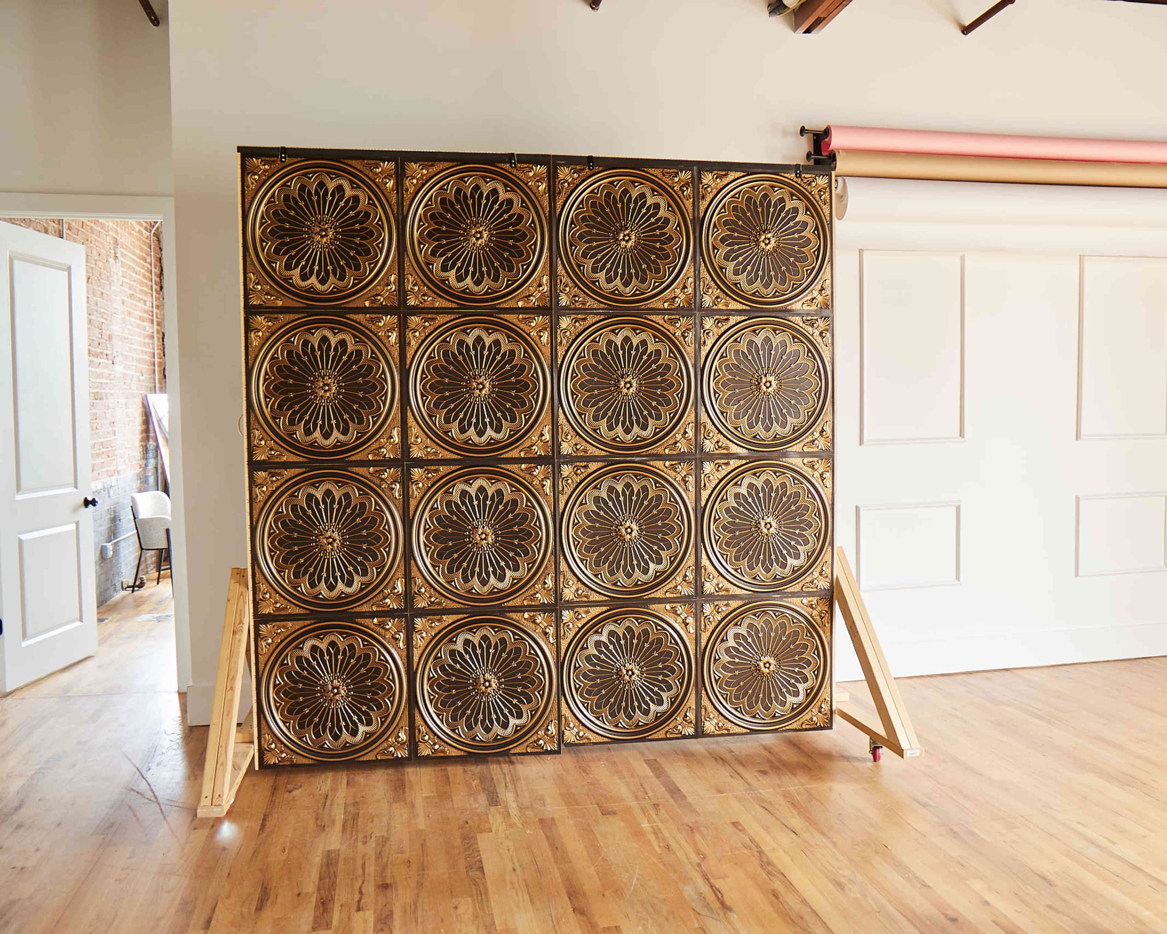 A patterned panel wall with circular designs, supported by woodenA-frames, in a room with wooden flooring and white walls.
