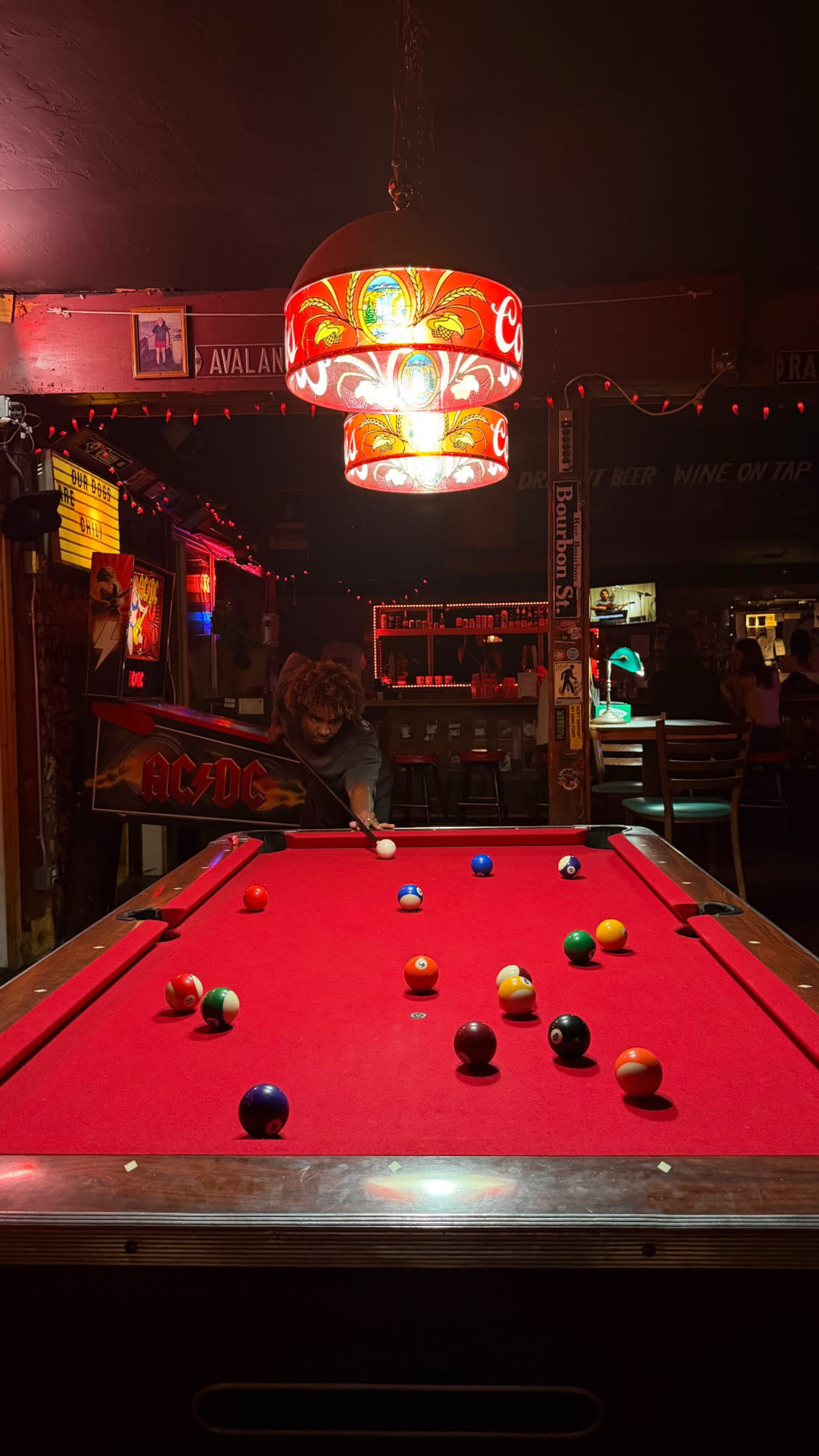 A person is playing billiards at a dimly lit bar with red neon lights and a vibrant pool table.