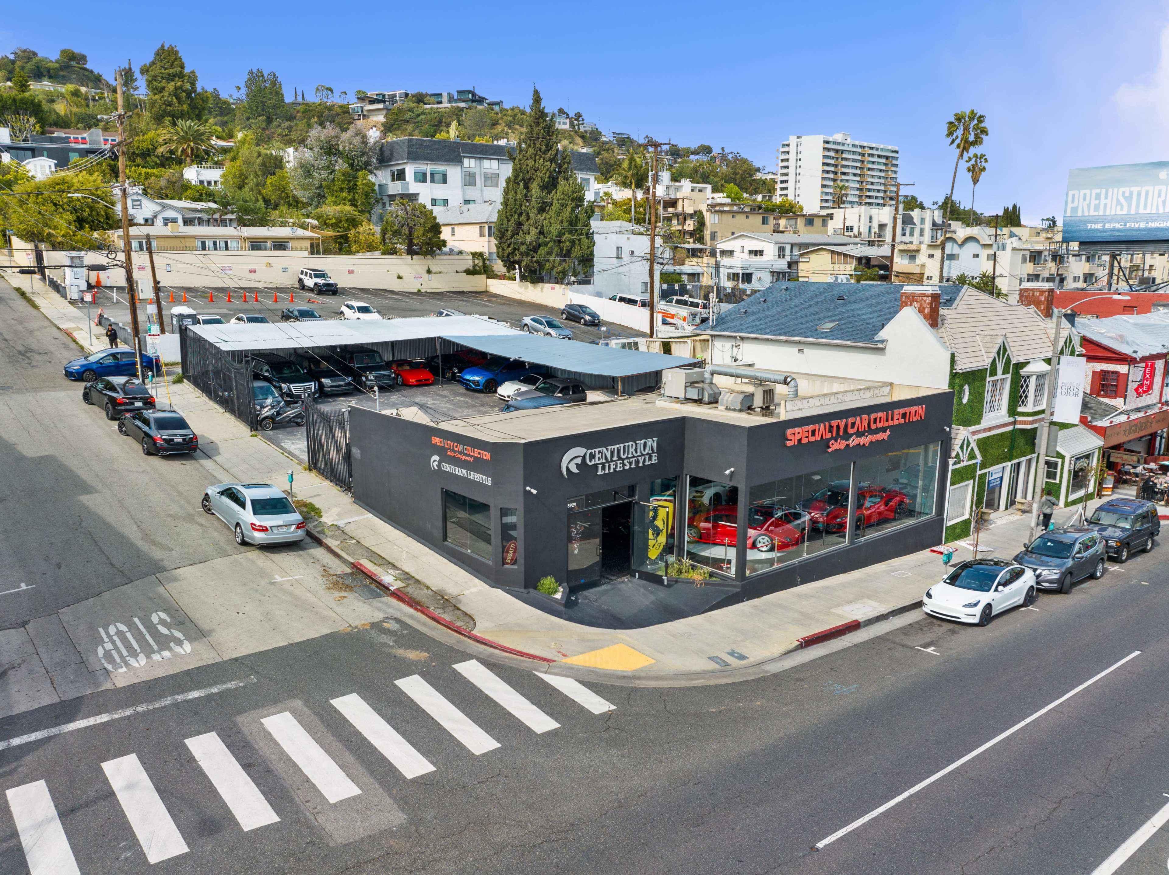 A modern car dealership building with a black exterior and a display of red cars in front, located on a busy street lined with residential and commercial buildings.