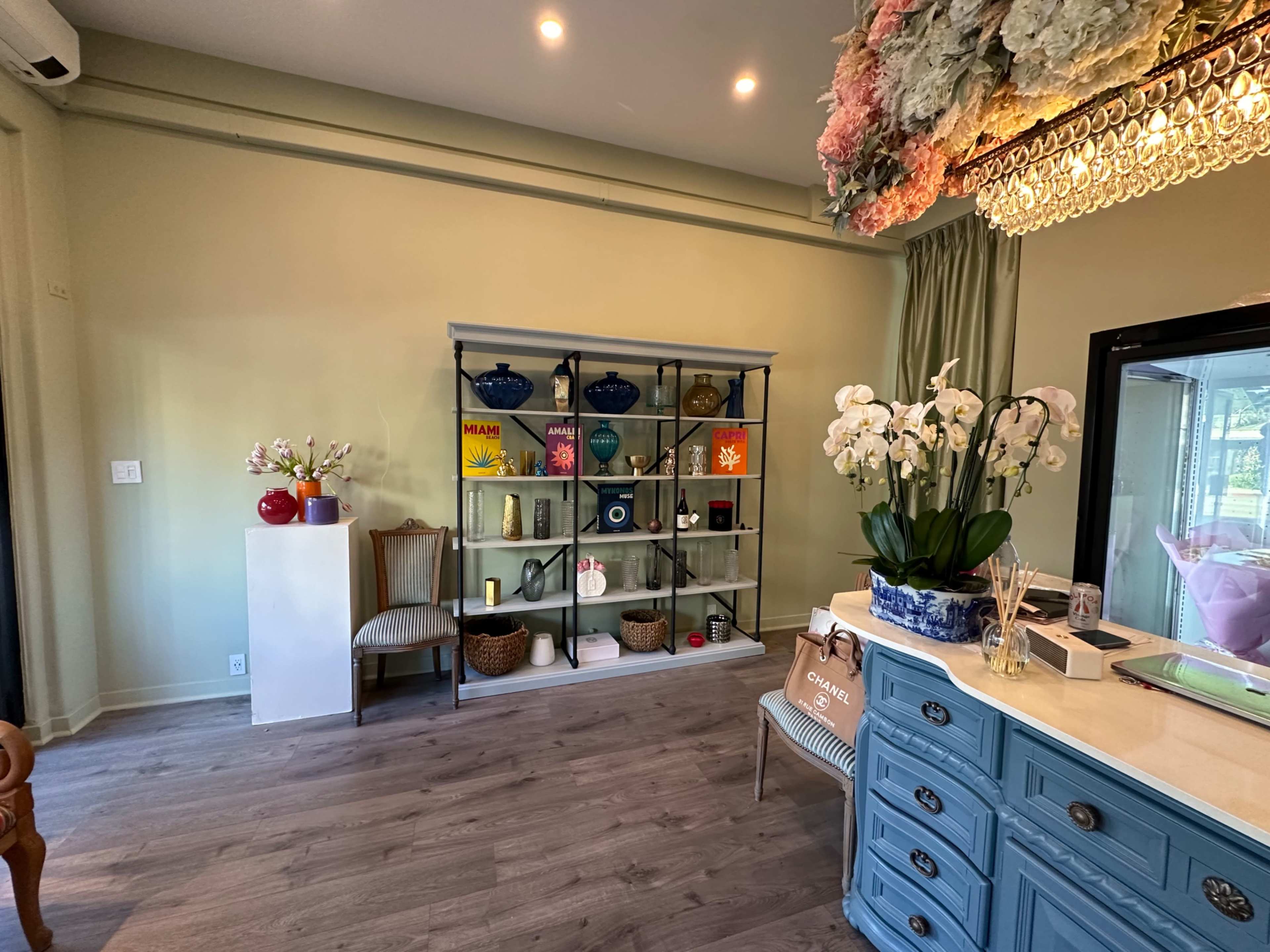 The room features a light green wall, a shelving unit filled with decorative items, and a side table with a vase of white orchids.