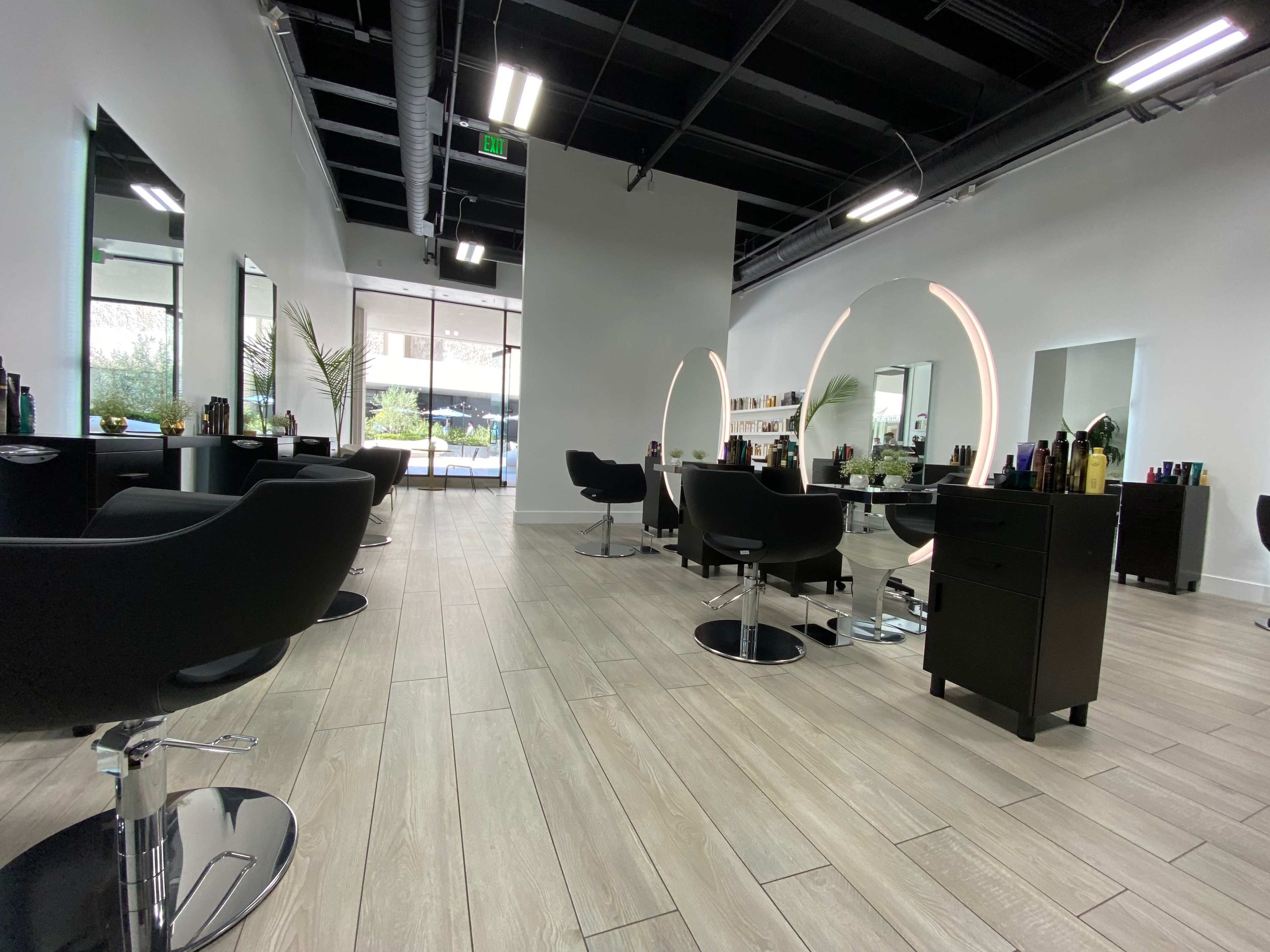 A modern hair salon with black styling chairs, large illuminated mirrors, and a minimalistic interior design.