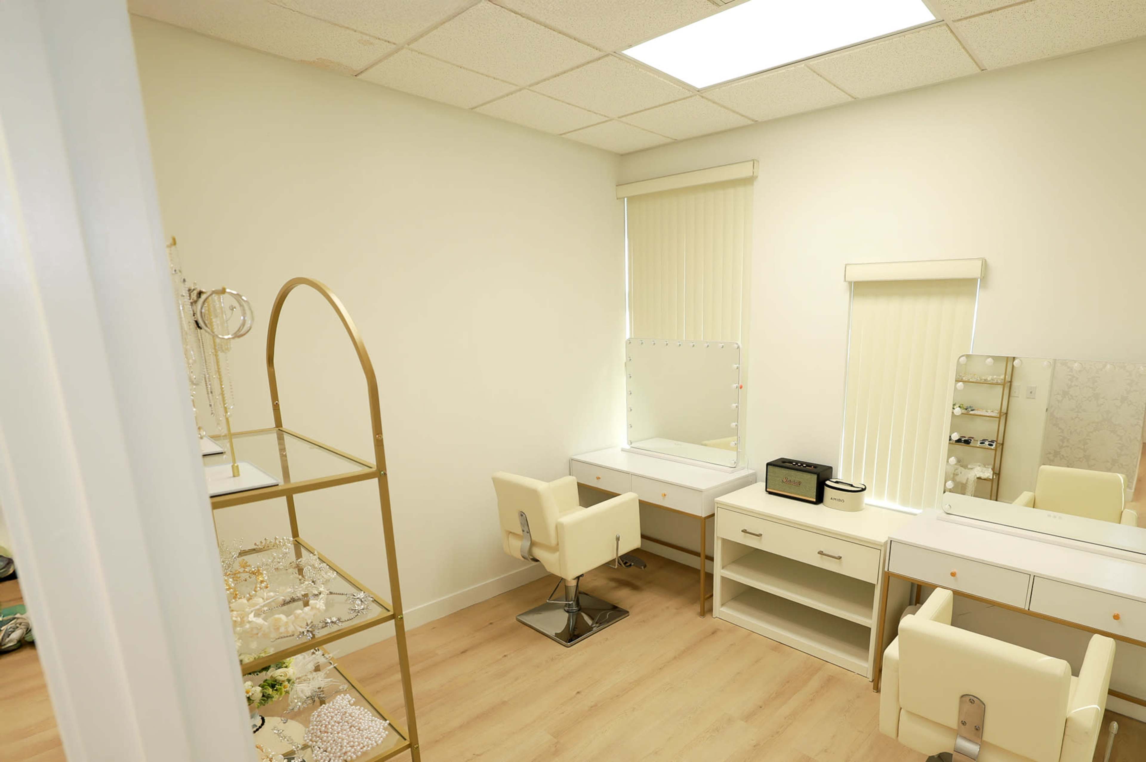 The image shows a bright room featuring a vanity area with two chairs, a mirror, and a display shelf for jewelry.