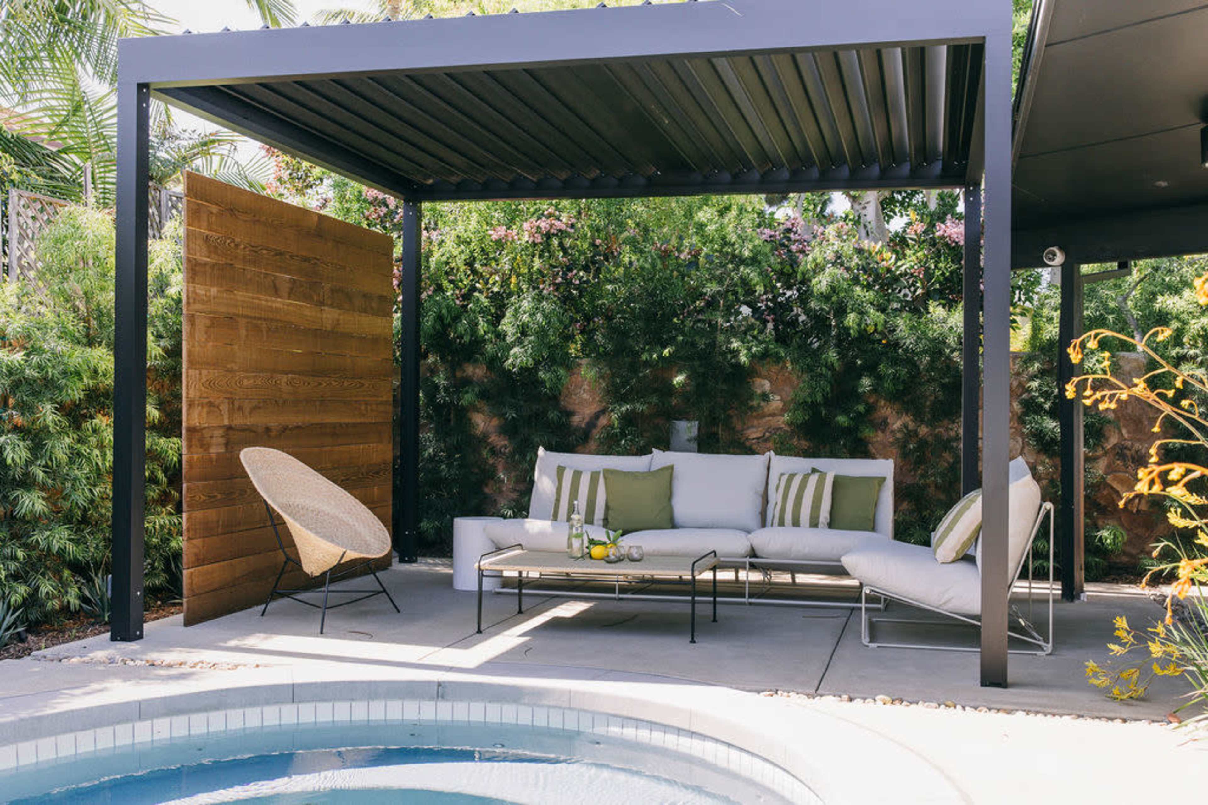 A shaded outdoor seating area features a modern sofa and armchair beside a small pool.