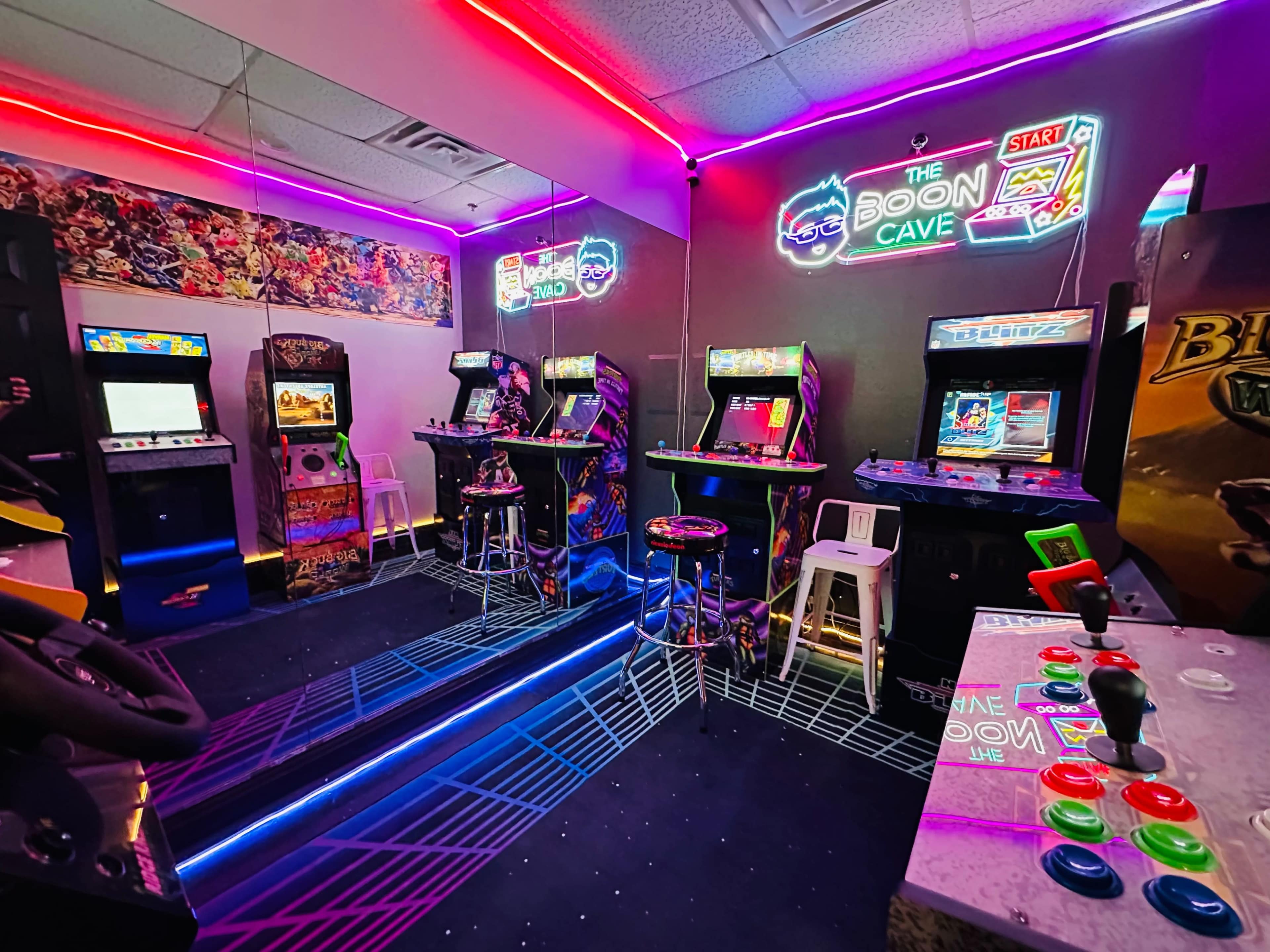 A neon-lit arcade room featuring vintage gaming machines, colorful stools, and a vibrant mural on the wall.