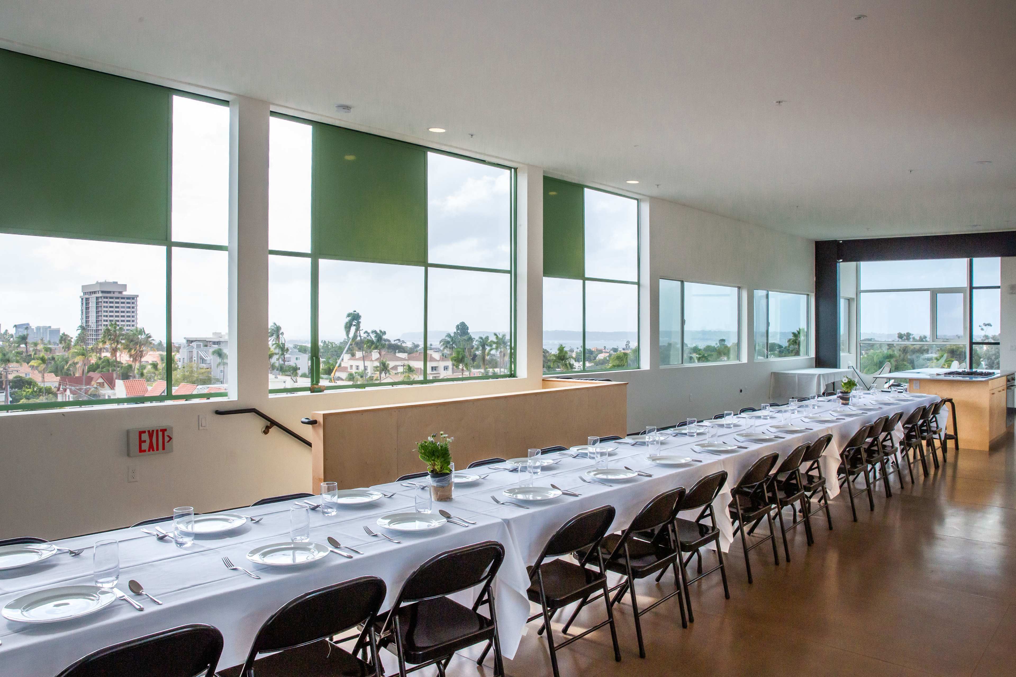 A long table set with plates and glasses is arranged by large windows overlooking a cityscape.
