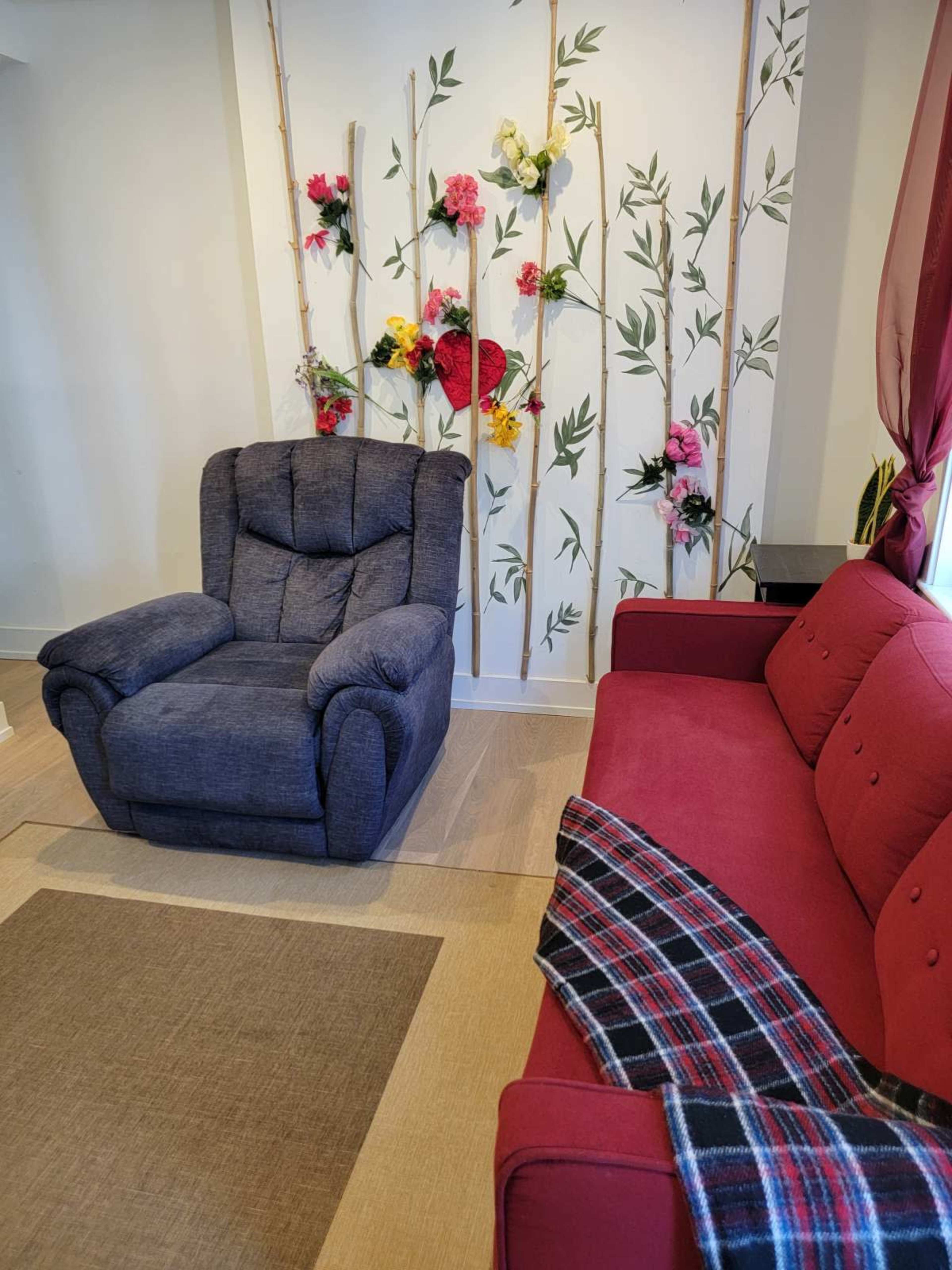 A blue recliner and a red sofa are positioned in a room with a decorative flower and bamboo wall.