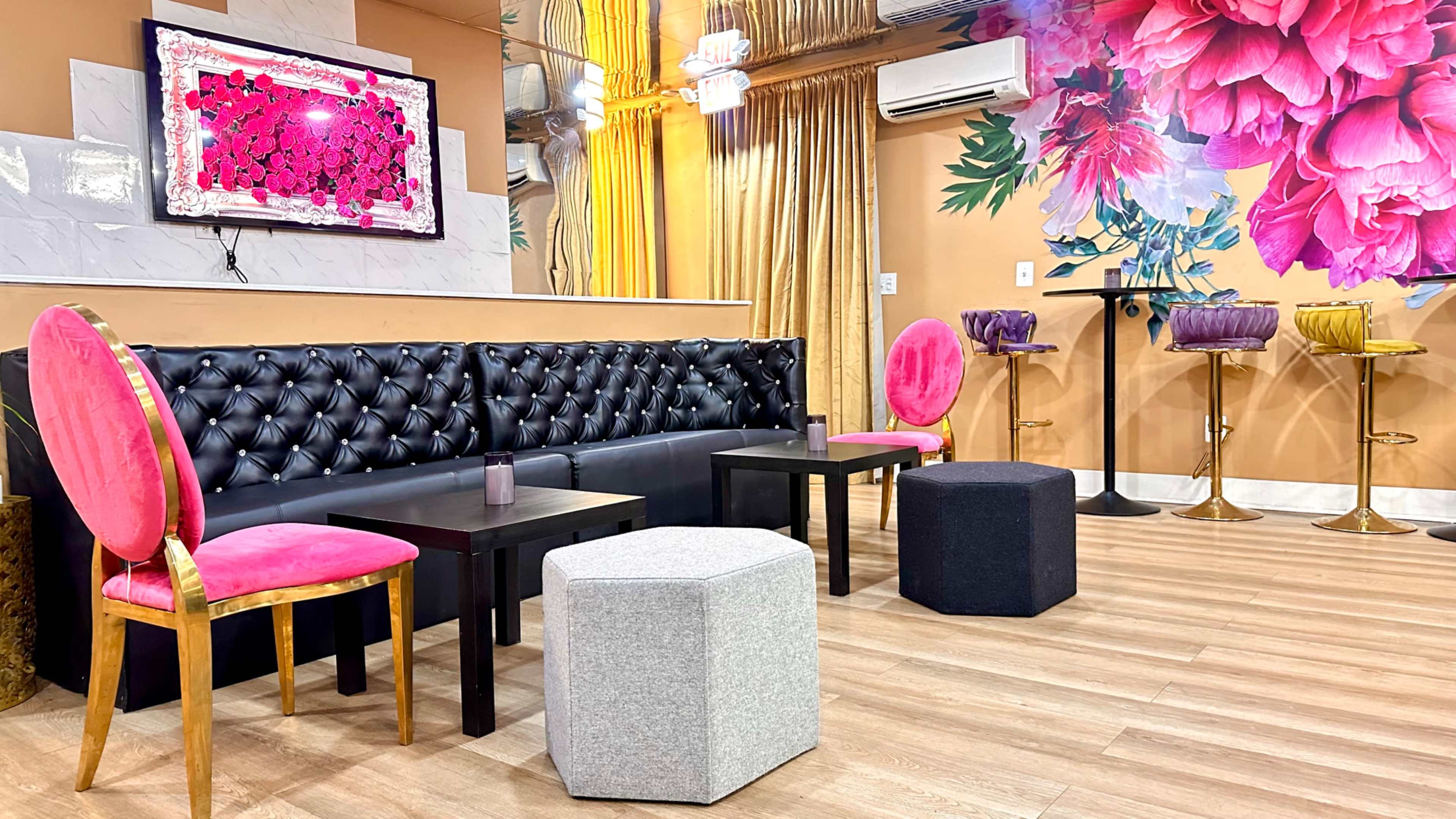 The image shows a stylish interior with black leather seating, pink chairs, and colorful floral decorations on the wall.