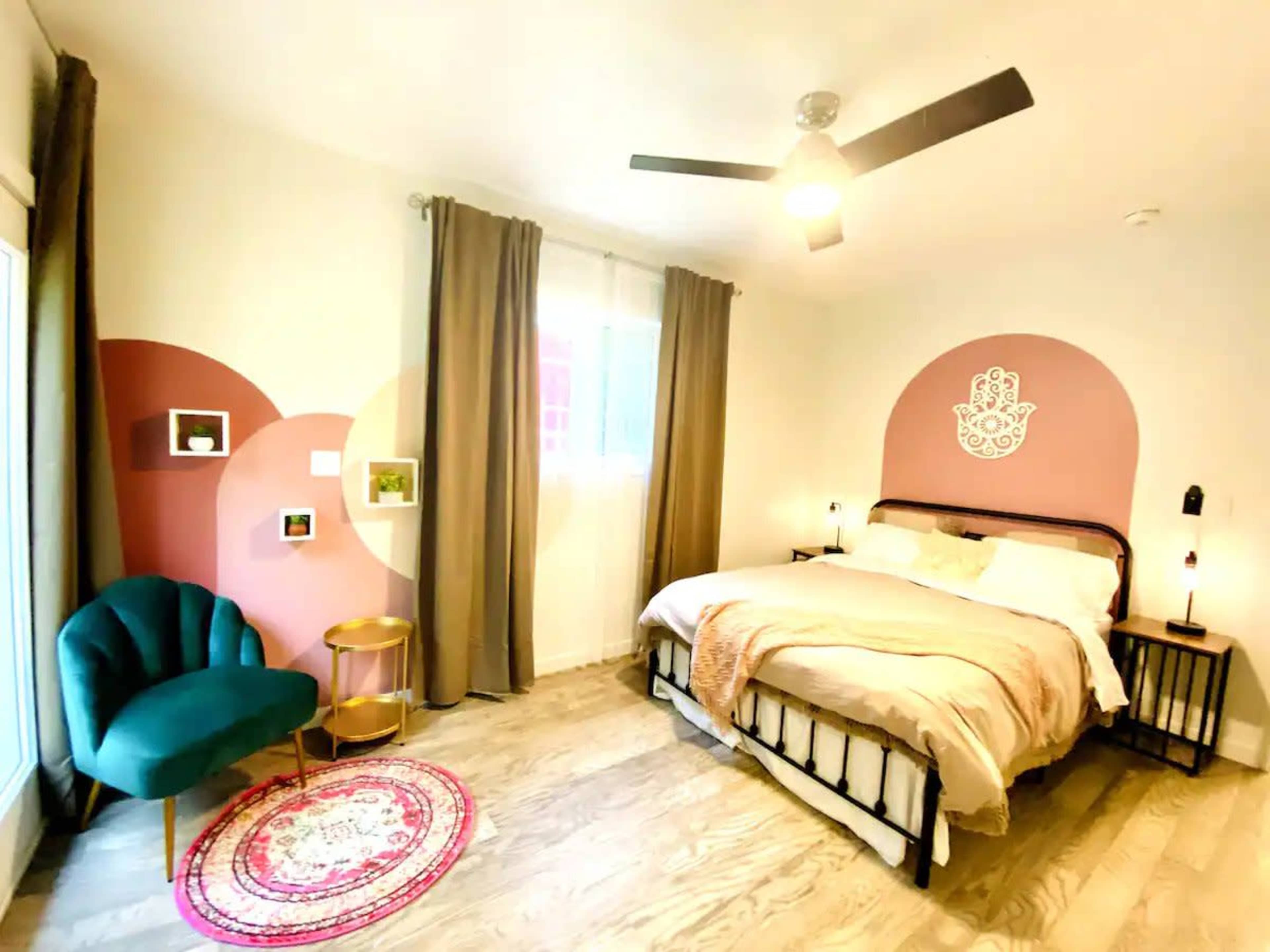 A modern bedroom with a bed, a green chair, decorative wall features, and a circular area rug on a wooden floor.