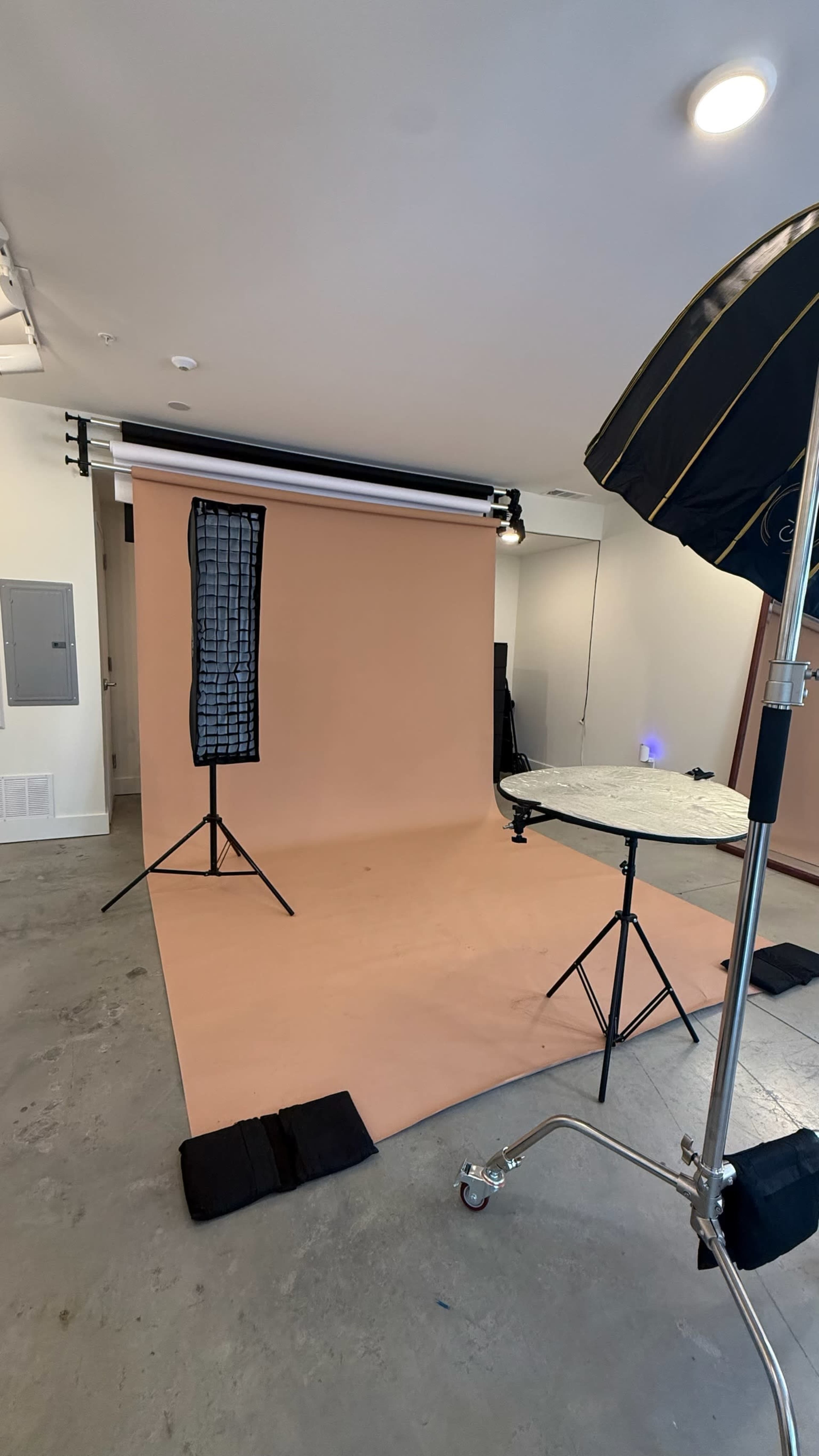 The image shows a photography studio with a seamless brown backdrop, two lighting stands, and a round table set up on a concrete floor.