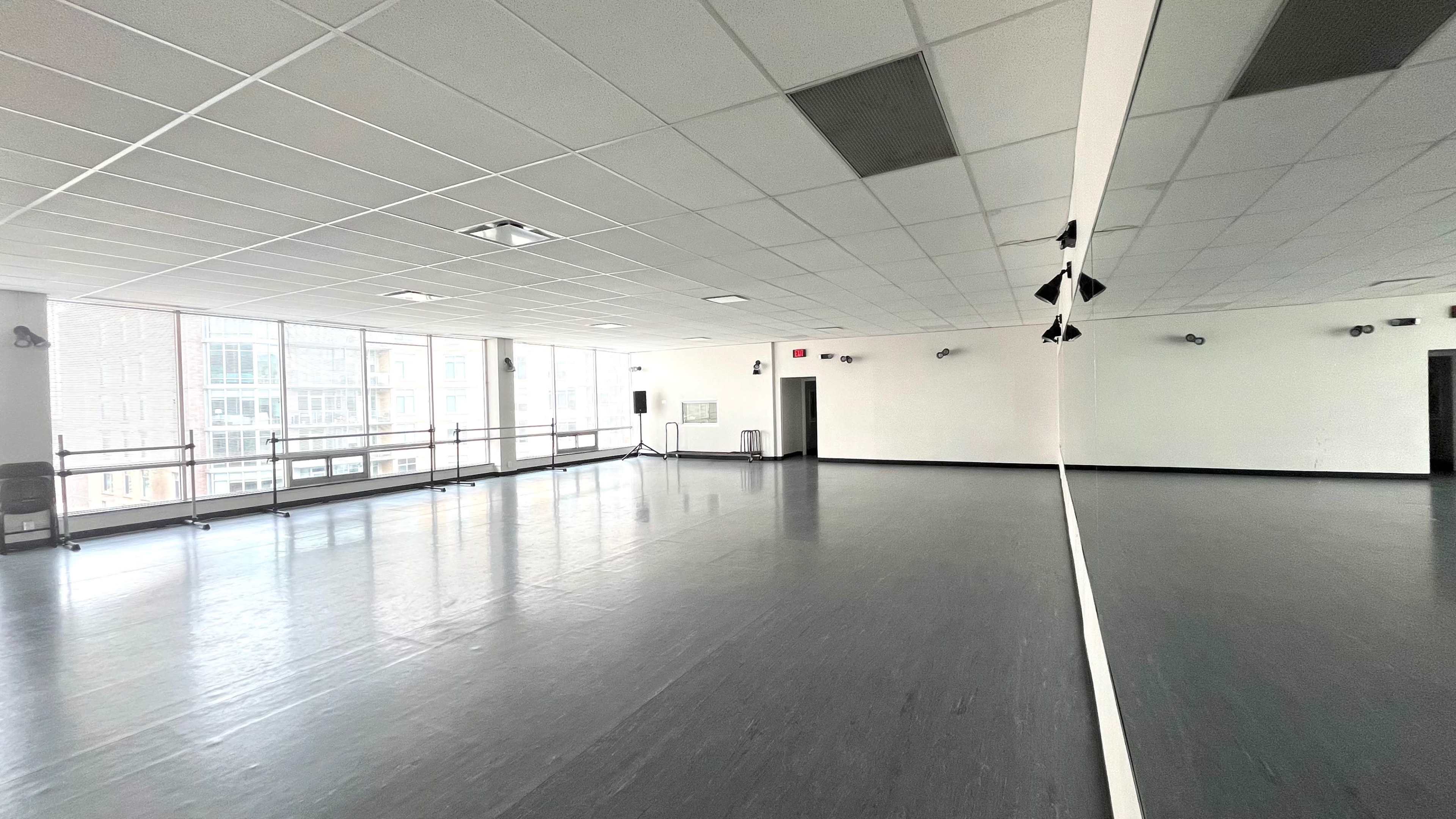 An empty dance studio with large windows and a mirrored wall.