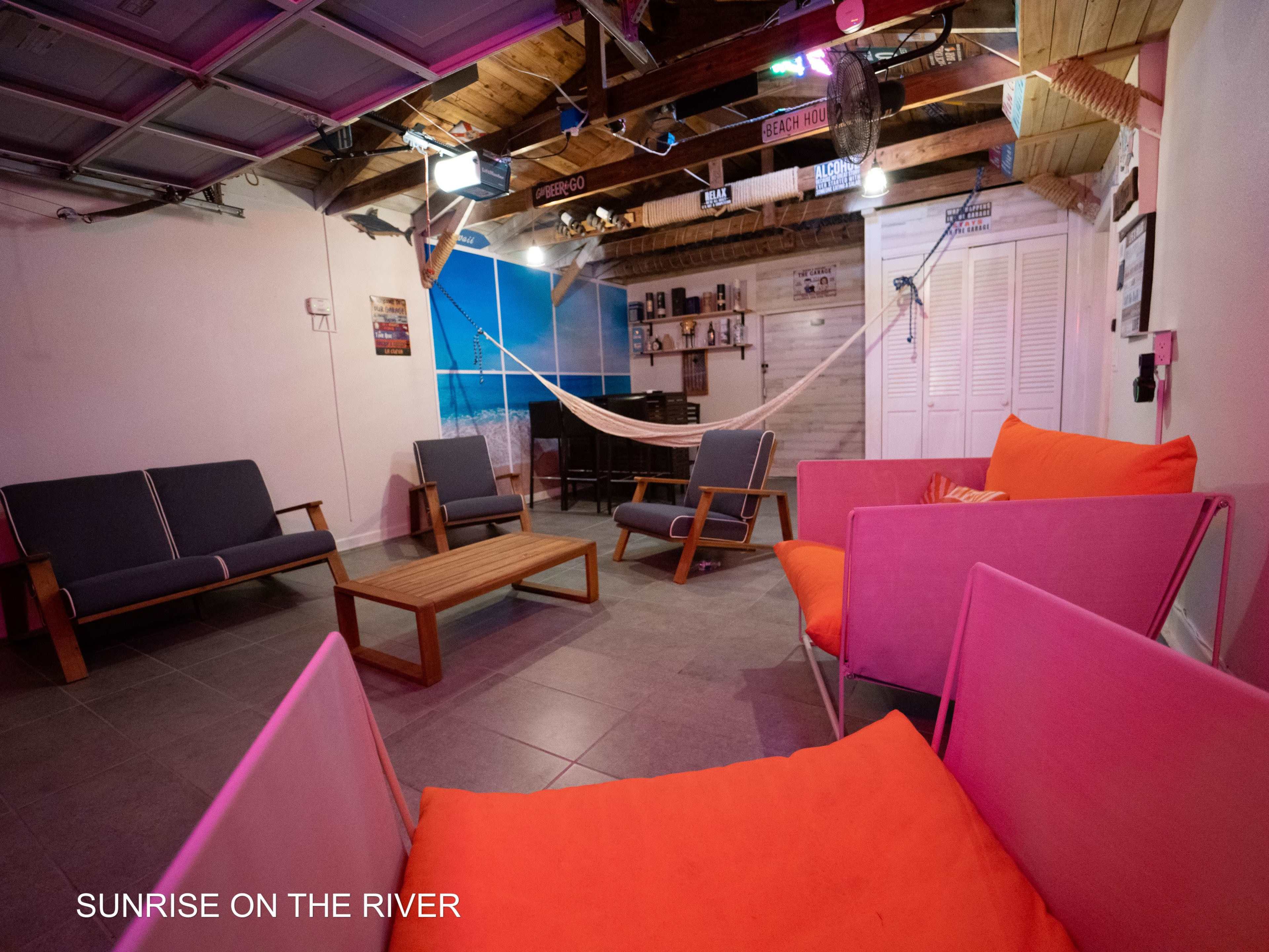 A casual lounge area with gray and pink seating, a wooden coffee table, and a hammock, set against a backdrop of beach-themed decor.