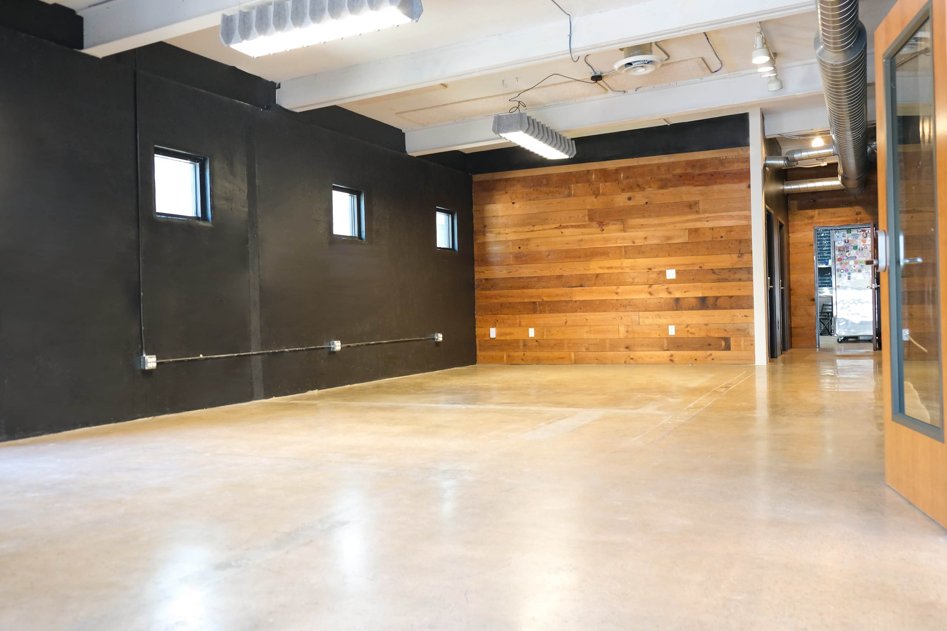The image shows a spacious interior with a polished concrete floor, black walls, and a wooden accent wall.