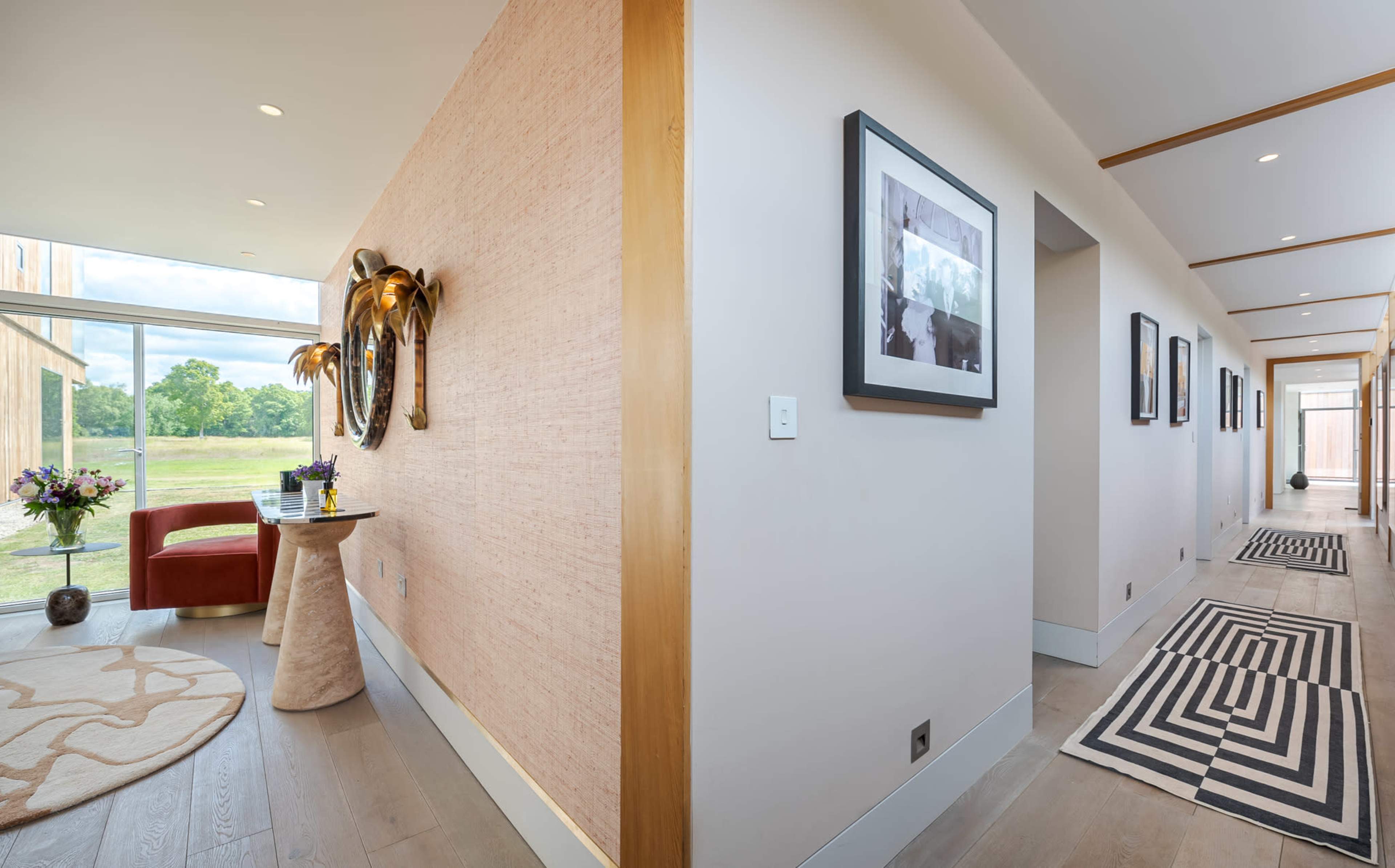 A hallway features a decorative table with a vase of flowers on one side and a series of framed photographs on the opposite wall.