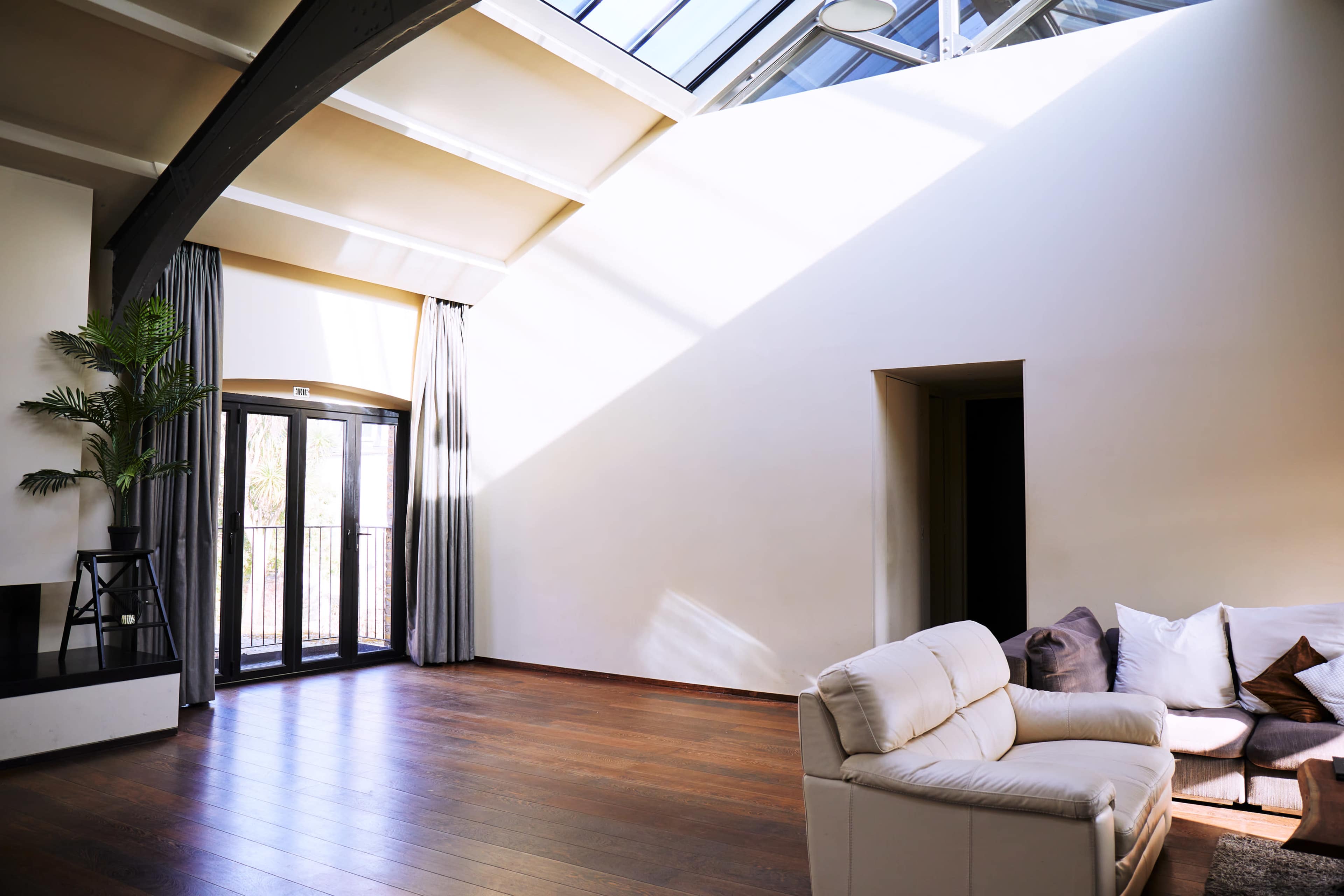 A spacious interior living area with large windows, wooden flooring, and a white sofa positioned against a wall.