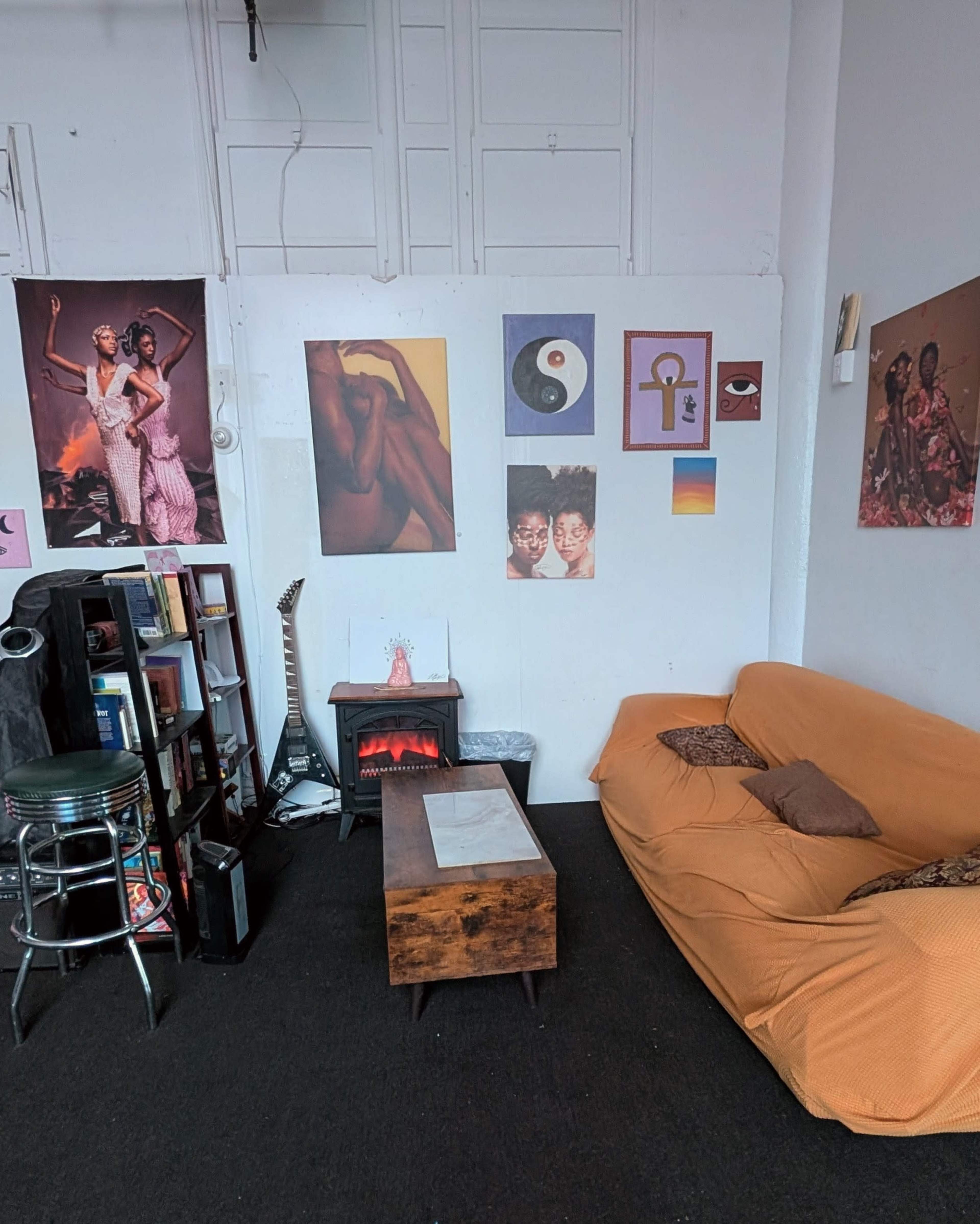 The image shows a cozy room with a large orange sofa, a wooden coffee table, bookshelves, and various colorful artworks displayed on the walls.