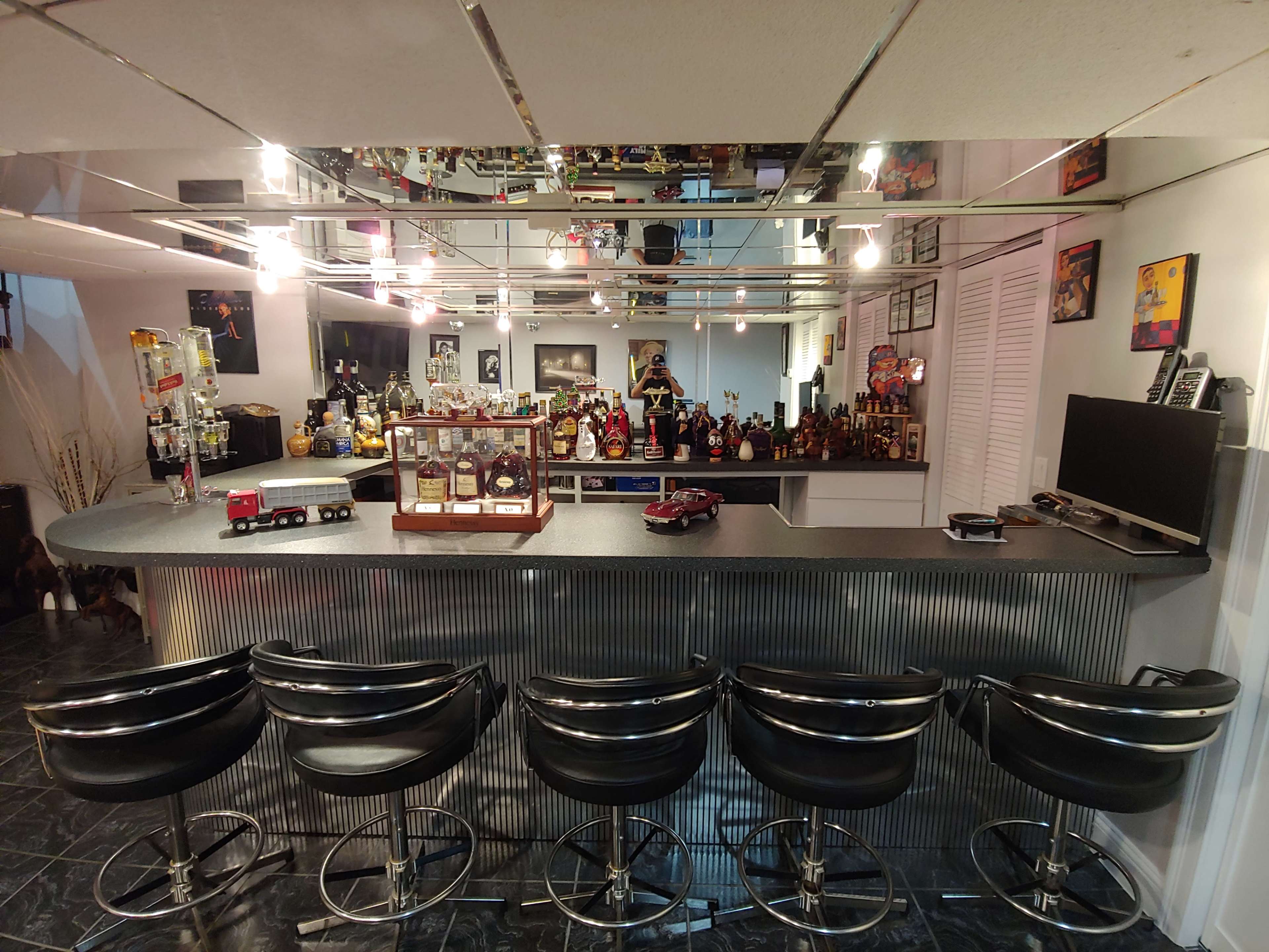 A stylish home bar with a curved counter, bar stools, and a display of various bottles and collectibles.