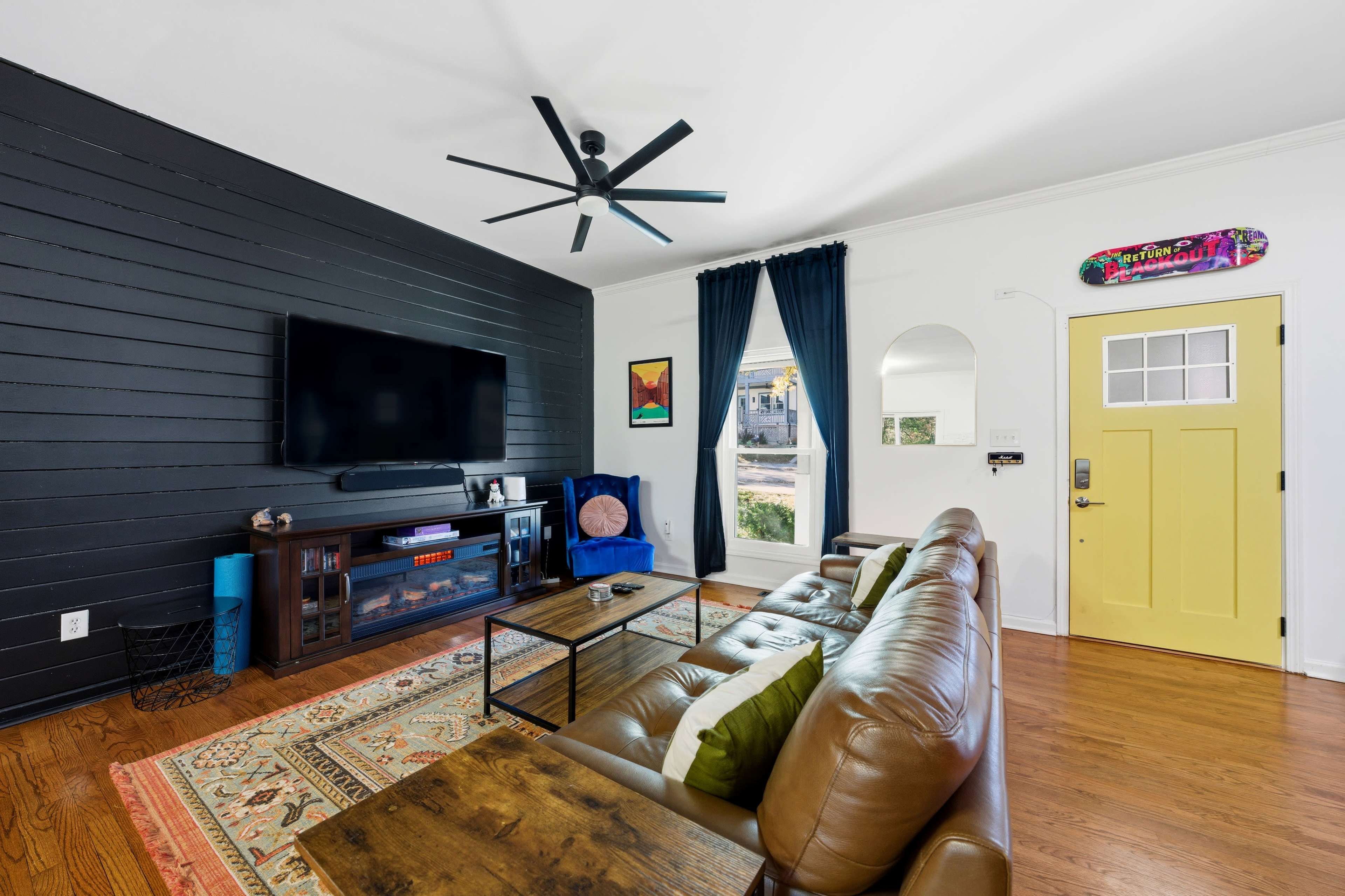 The living room features a black accent wall, a large TV mounted above a wooden media console, and a yellow door with a window.