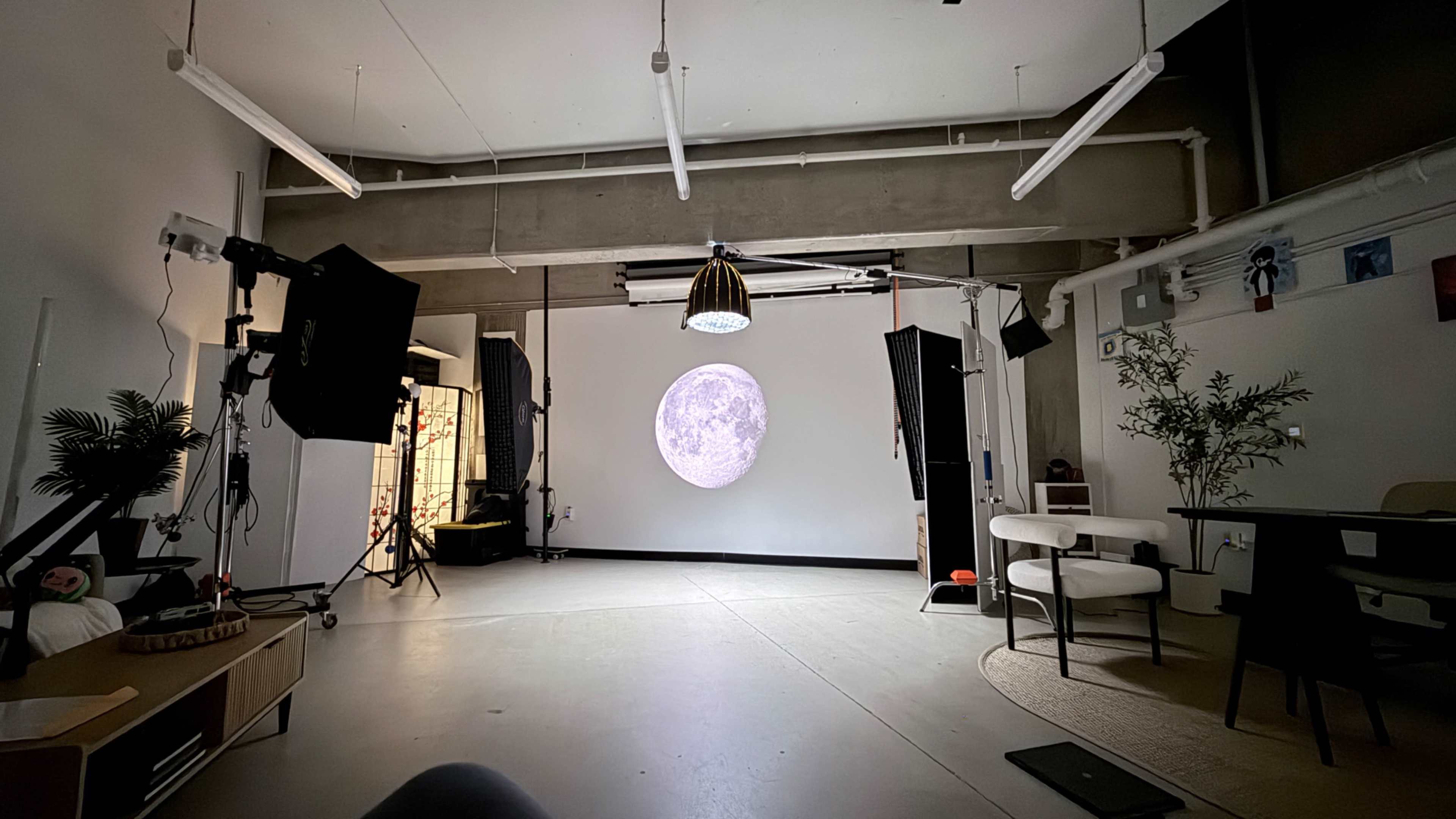The scene features a large, illuminated image of the moon projected on a white wall in a spacious room equipped with studio lighting and furniture.