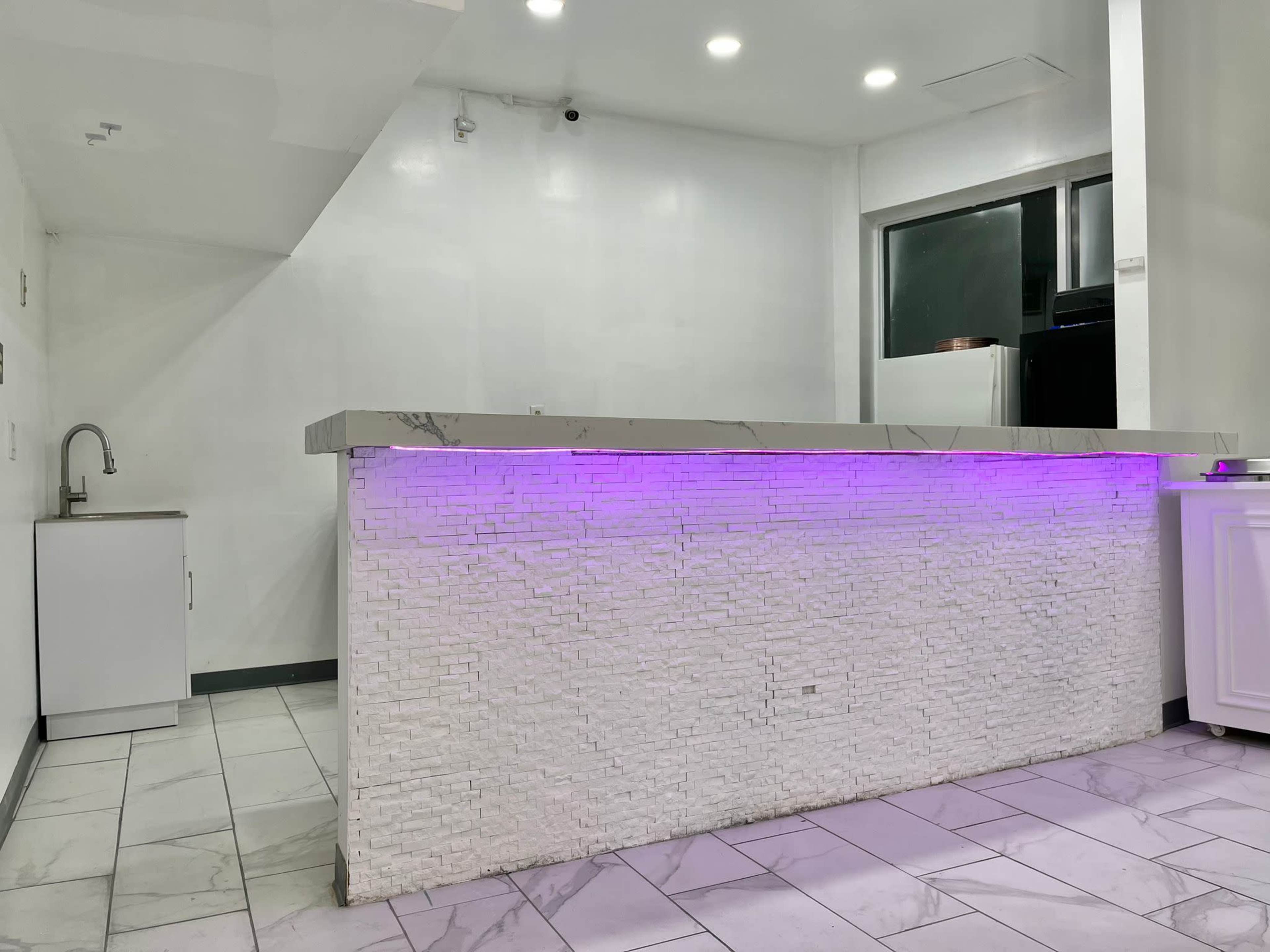 A modern reception area features a white stone bar with purple lighting and tiled flooring.