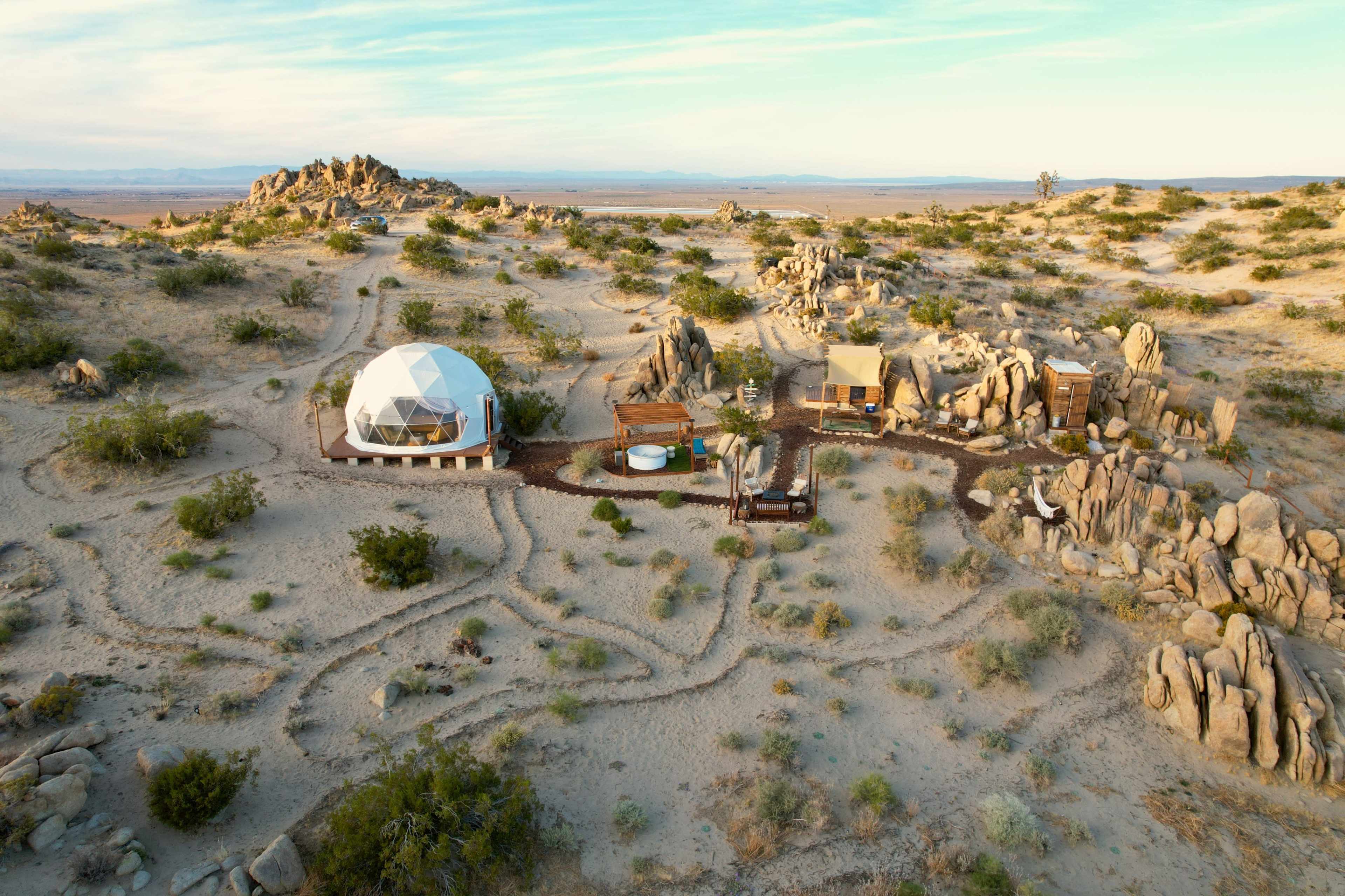 The image shows a geodesic dome structure surrounded by several small buildings and pathways in a rocky desert landscape.