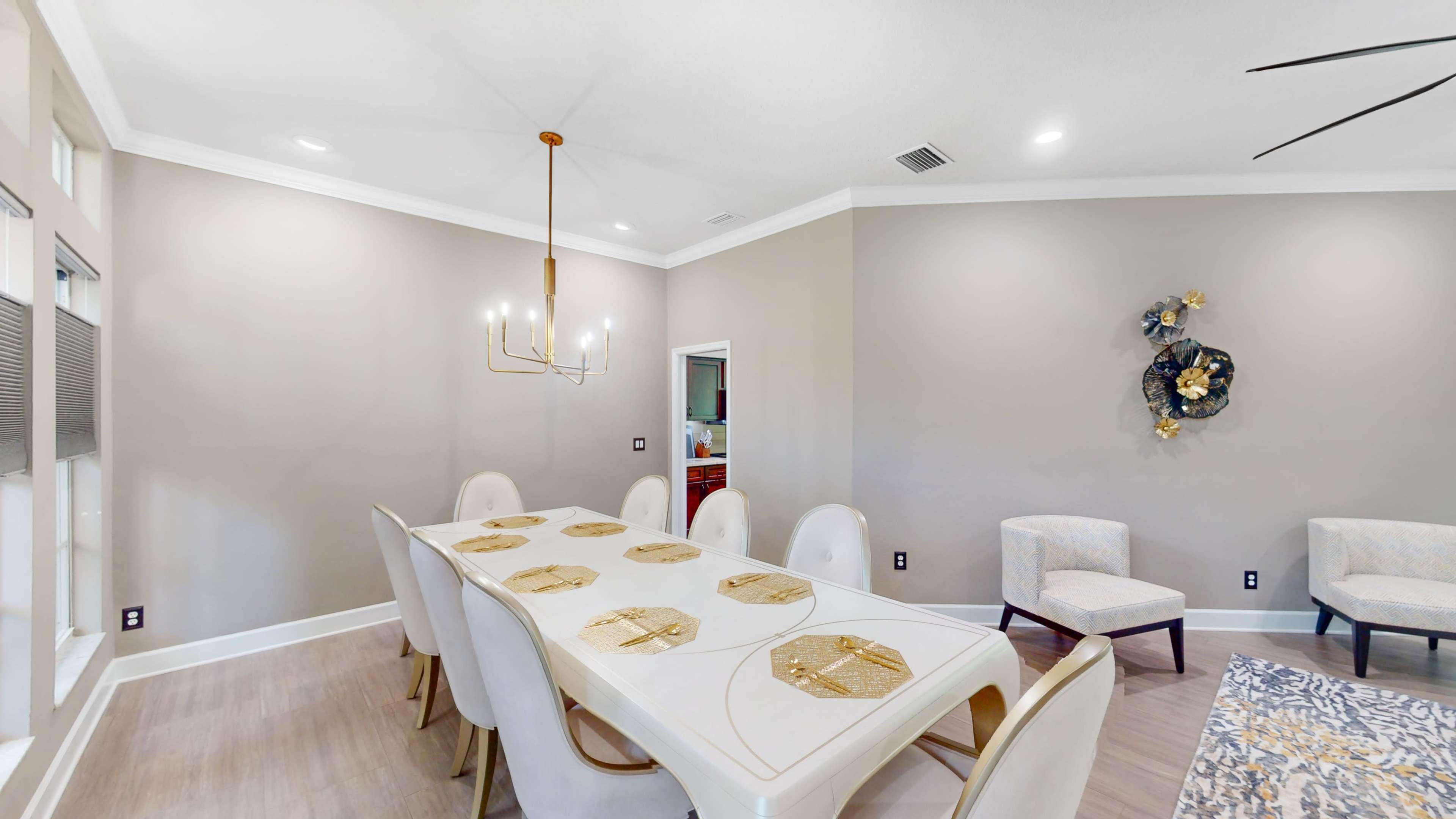 A modern dining room with a large white table set for eight, surrounded by upholstered chairs, and featuring a chandelier overhead.