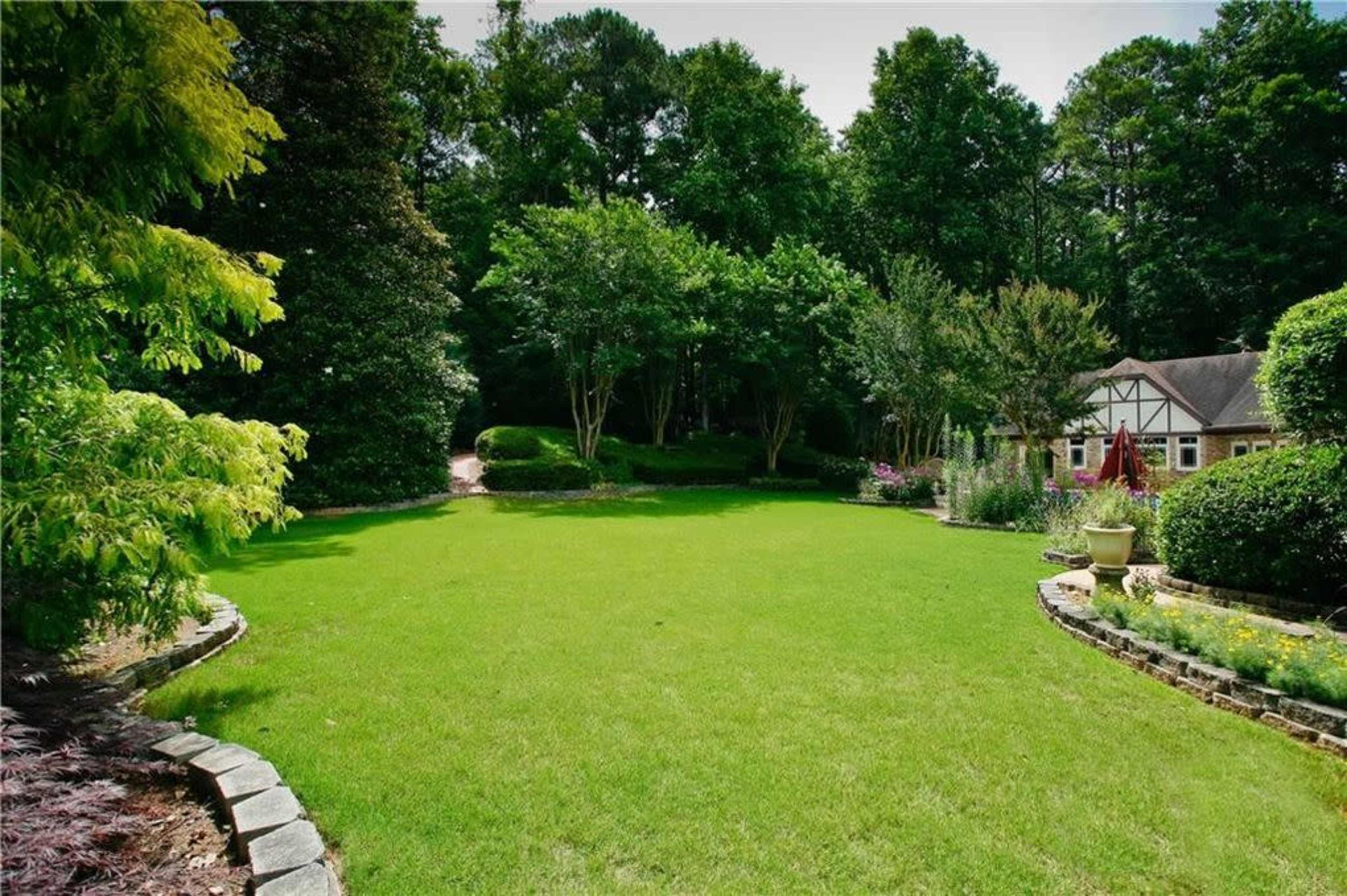 A well-maintained green lawn surrounded by trees and bushes, with a house visible in the background.