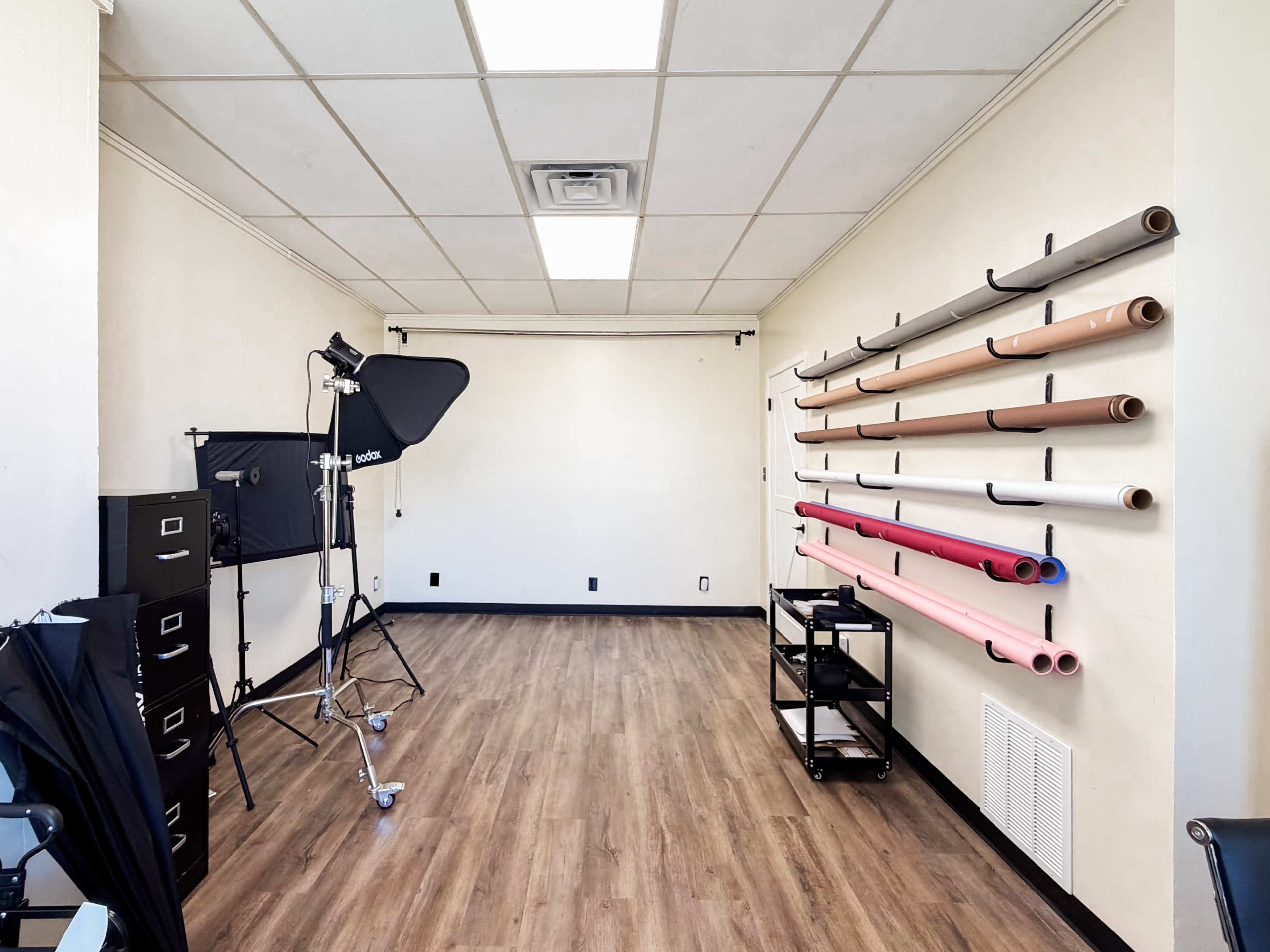 The image shows a photography studio with a backdrop support system, lighting equipment, and a wall-mounted rack holding various colored paper rolls.
