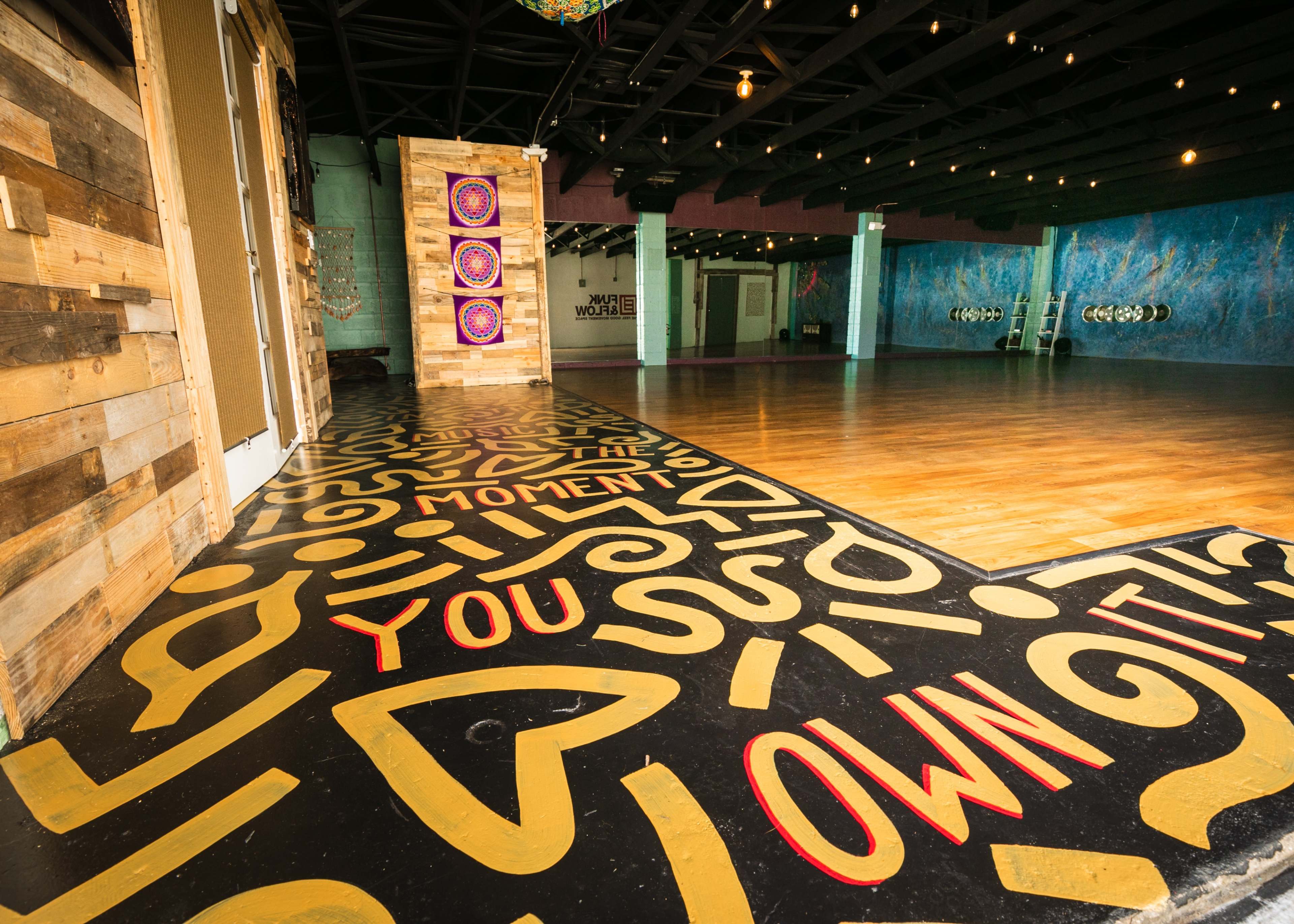A spacious room with a wooden floor and walls decorated with colorful patterns and inspirational phrases on the floor.