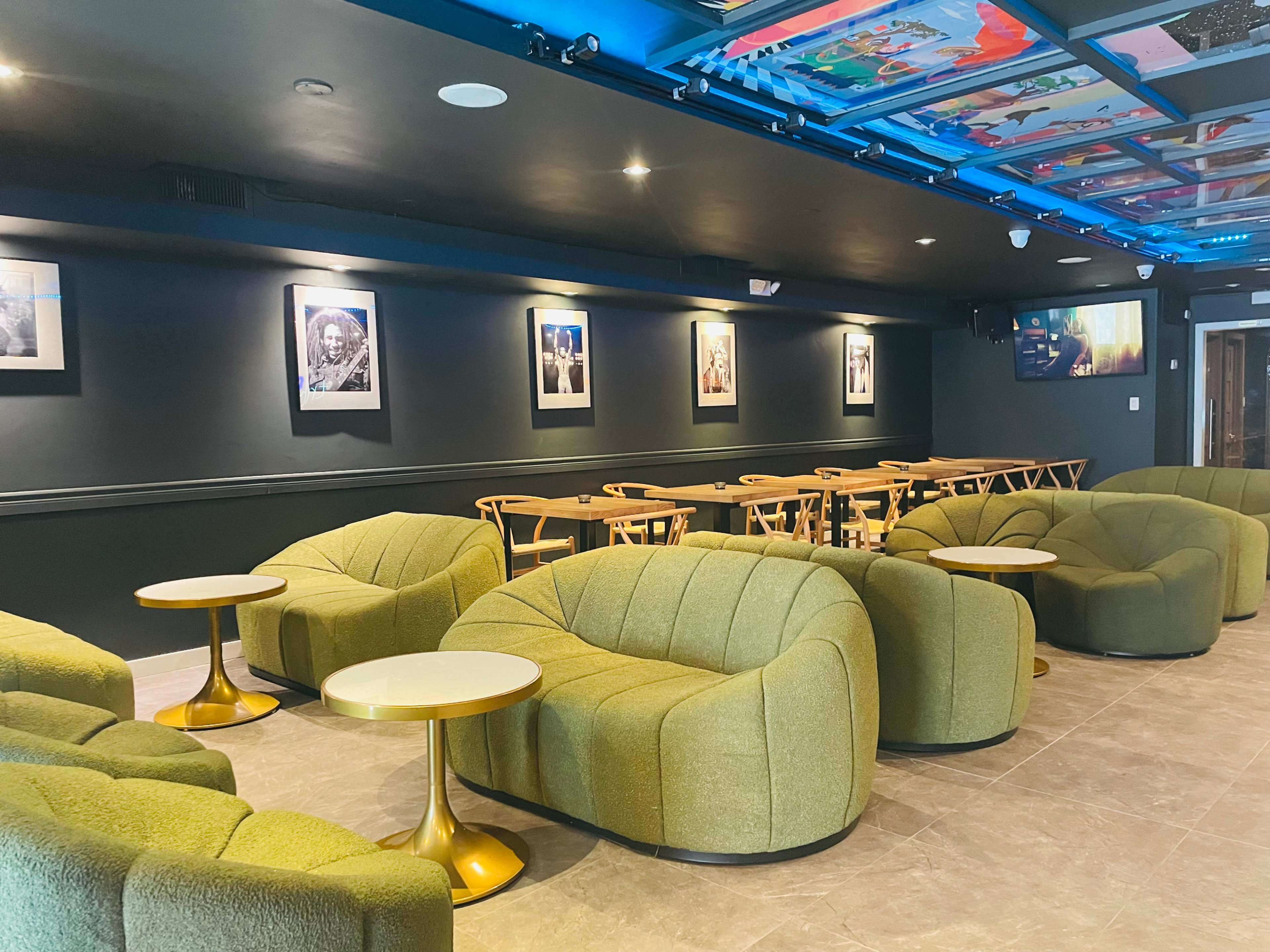 A modern interior of a café or lounge featuring green, curved seating, small round tables, and framed photographs on the walls.